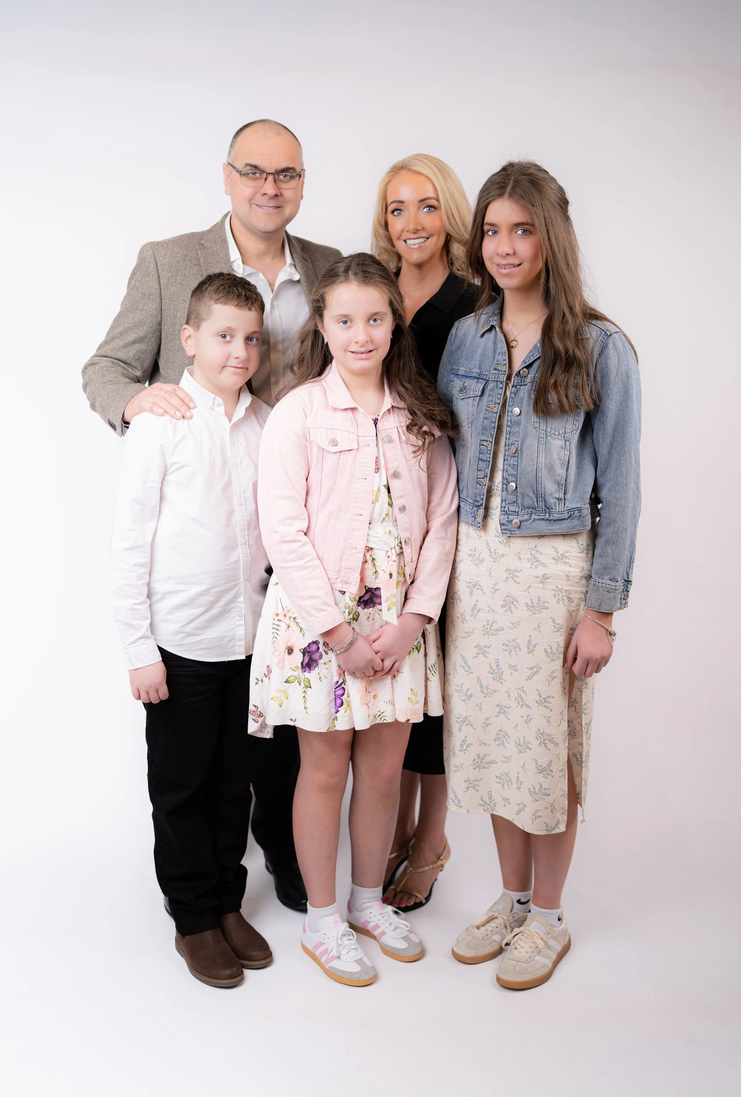 Two young boys with brown hair and dressed in casual matching t-shirts and leggings, one standing and one sitting on a wooden ladder, against a dark gray studio background.