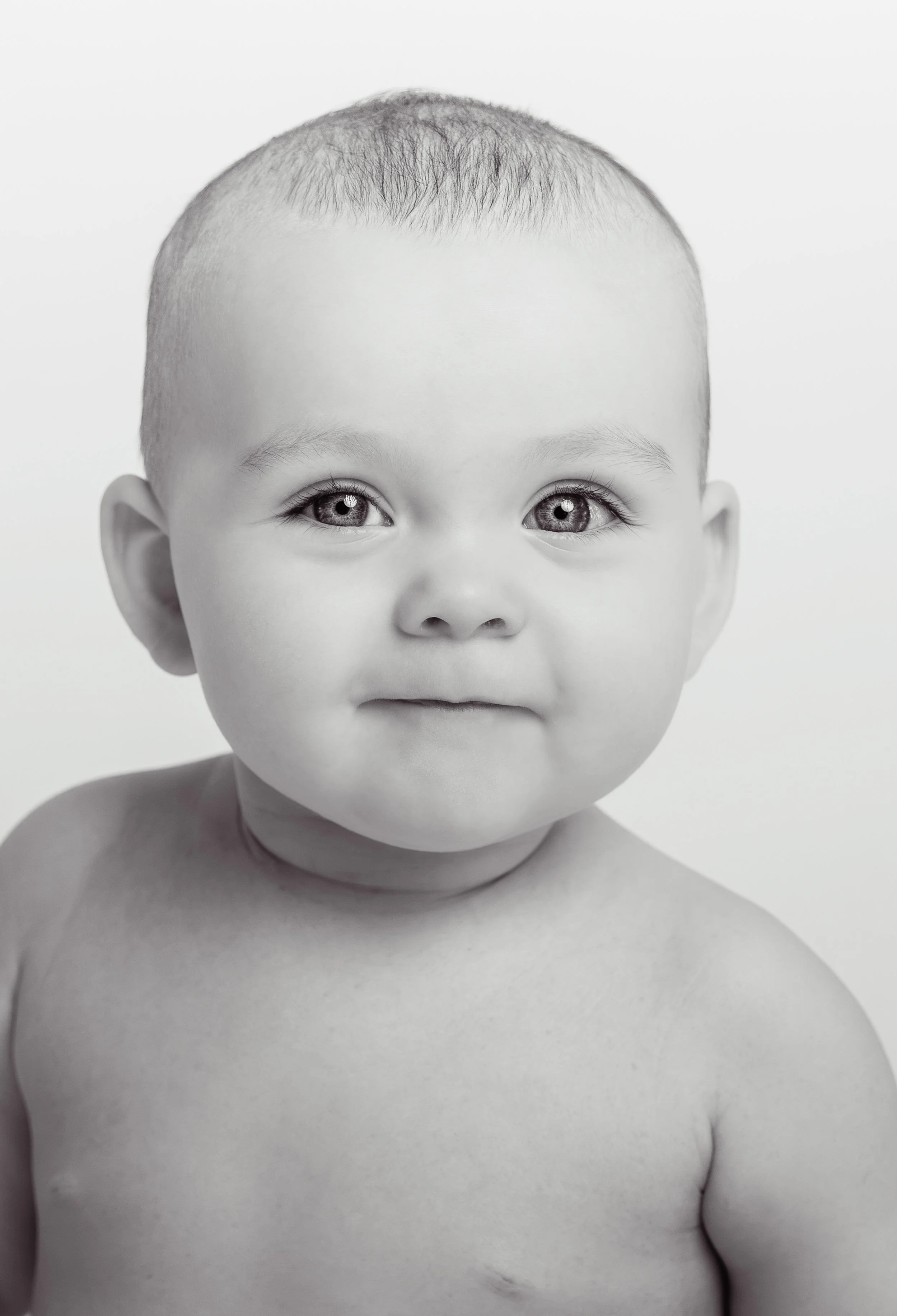 Black-and-white portrait of a young child with a round face, short hair, and wide eyes, looking directly at the camera.