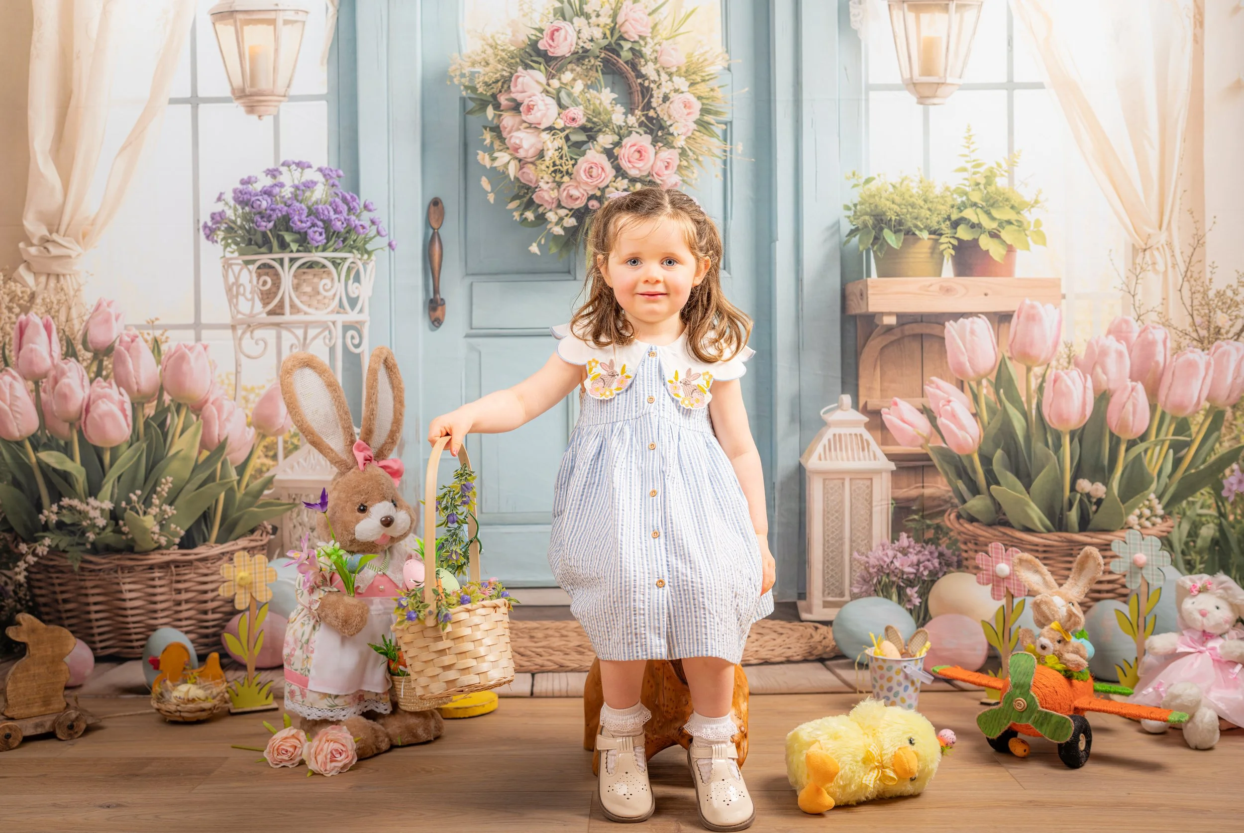 A young girl standing in a room decorated with spring flowers, bunny toys, and pastel-colored decorations, holding a bunny plush toy with flowers.