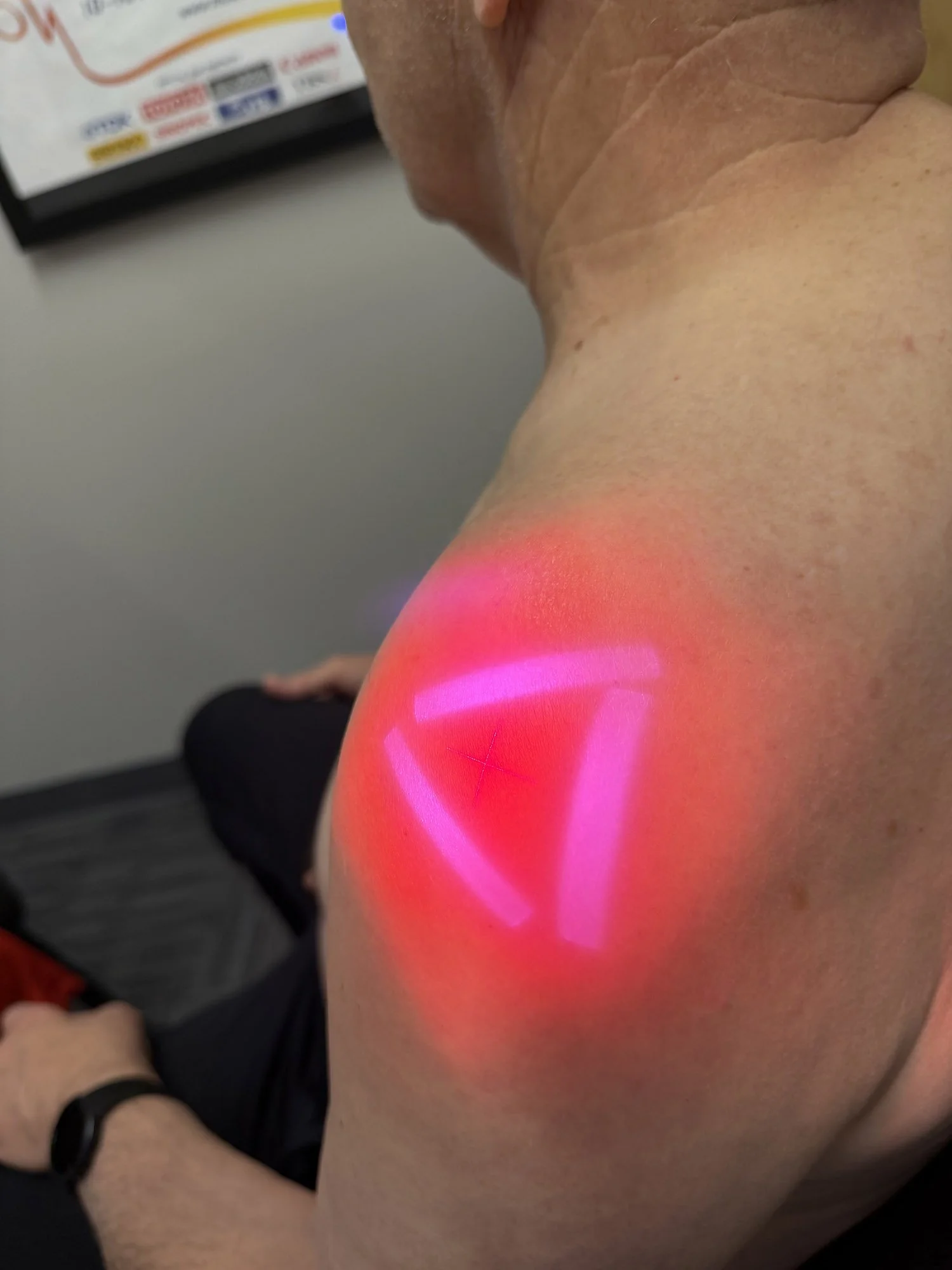 A person receiving a red light therapy treatment on their shoulder or upper arm.