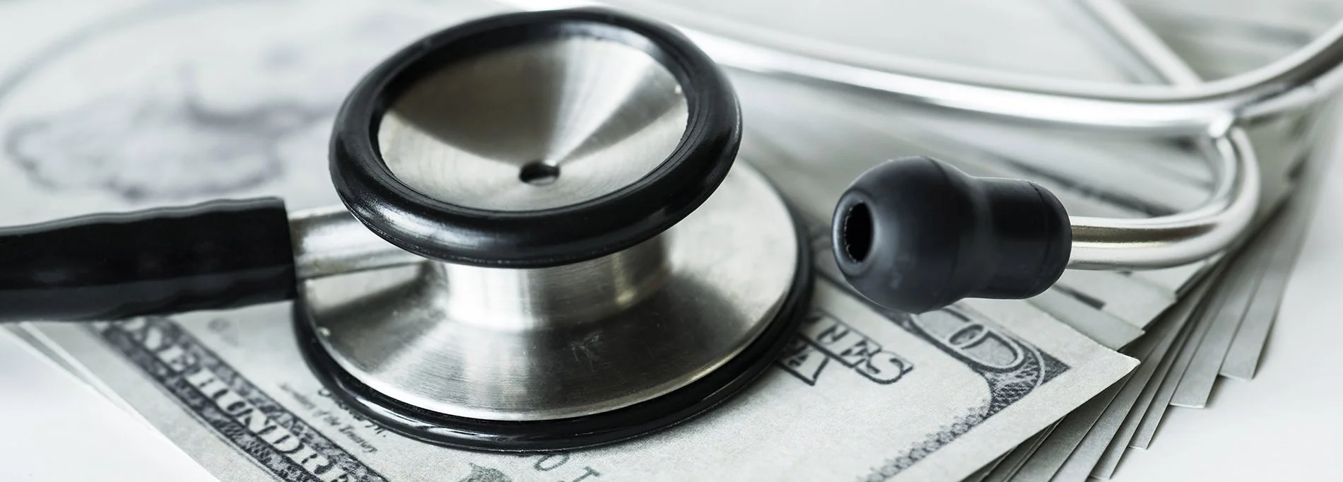 A stethoscope resting on top of a stack of hundred dollar bills.