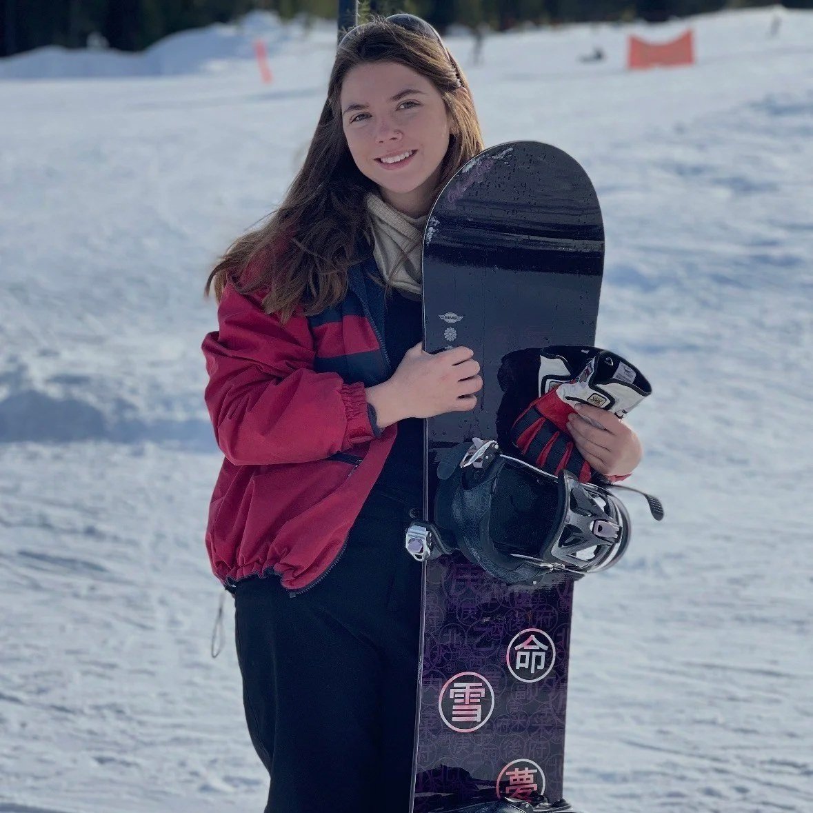 Young woman in winter gear holding snowboard and gloves on snowy mountain.