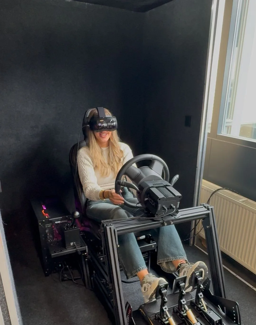 A woman with black hair smiling in a greenhouse surrounded by green plants.