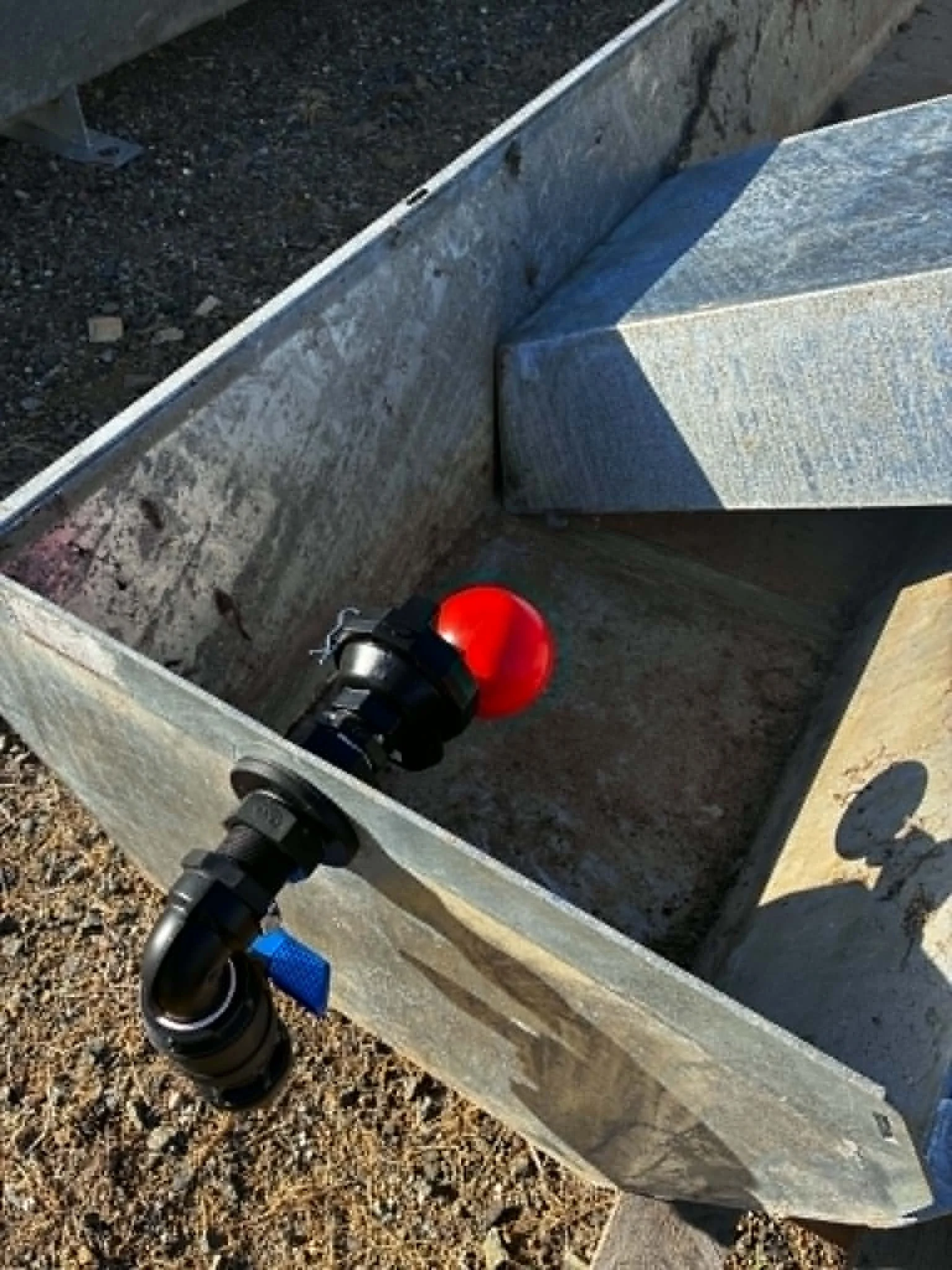 Close-up image of a metallic box with a propane torch attached to the side, situated on a gravel surface.