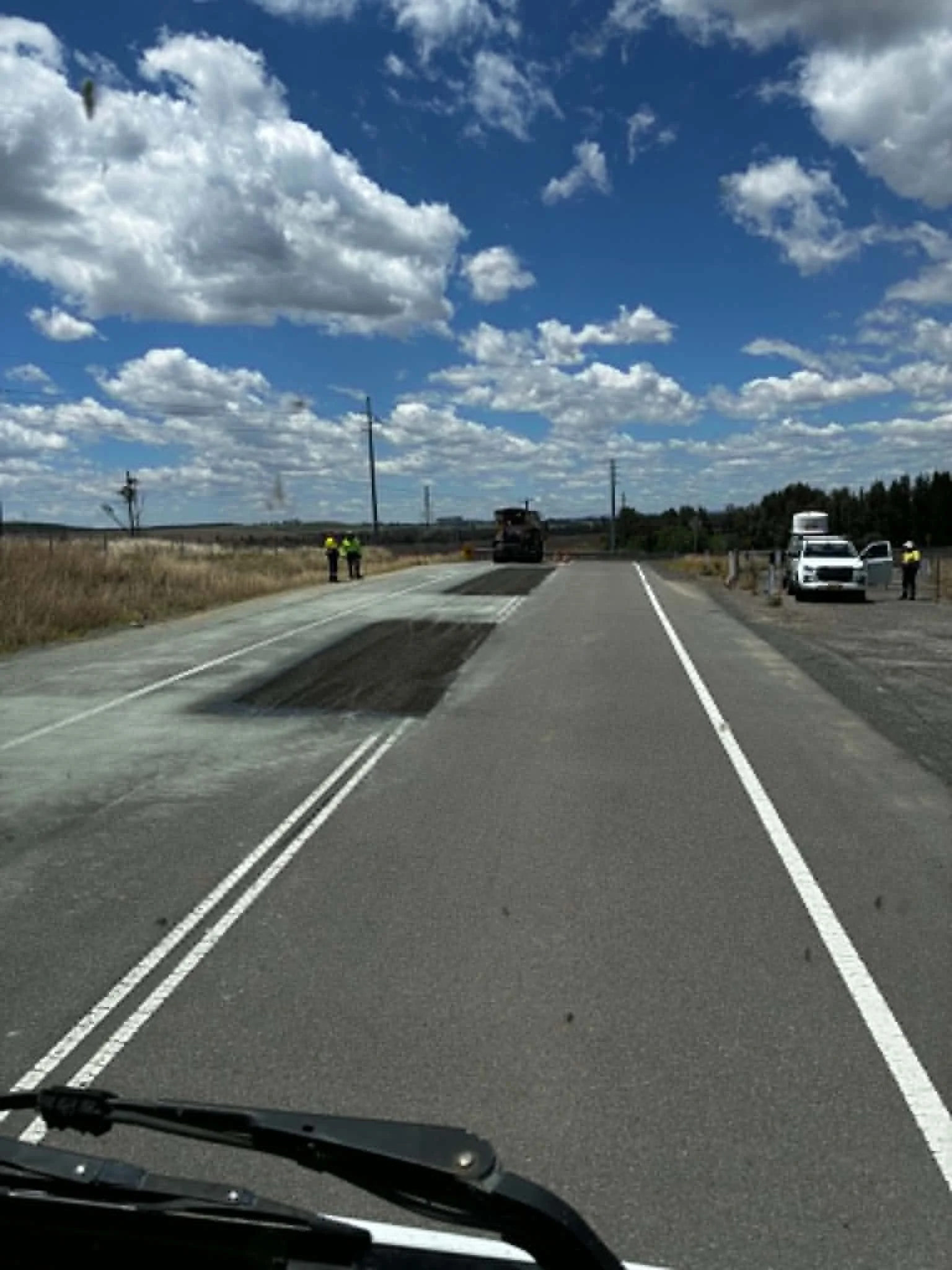 Road under construction with workers and vehicles, blue sky with clouds.