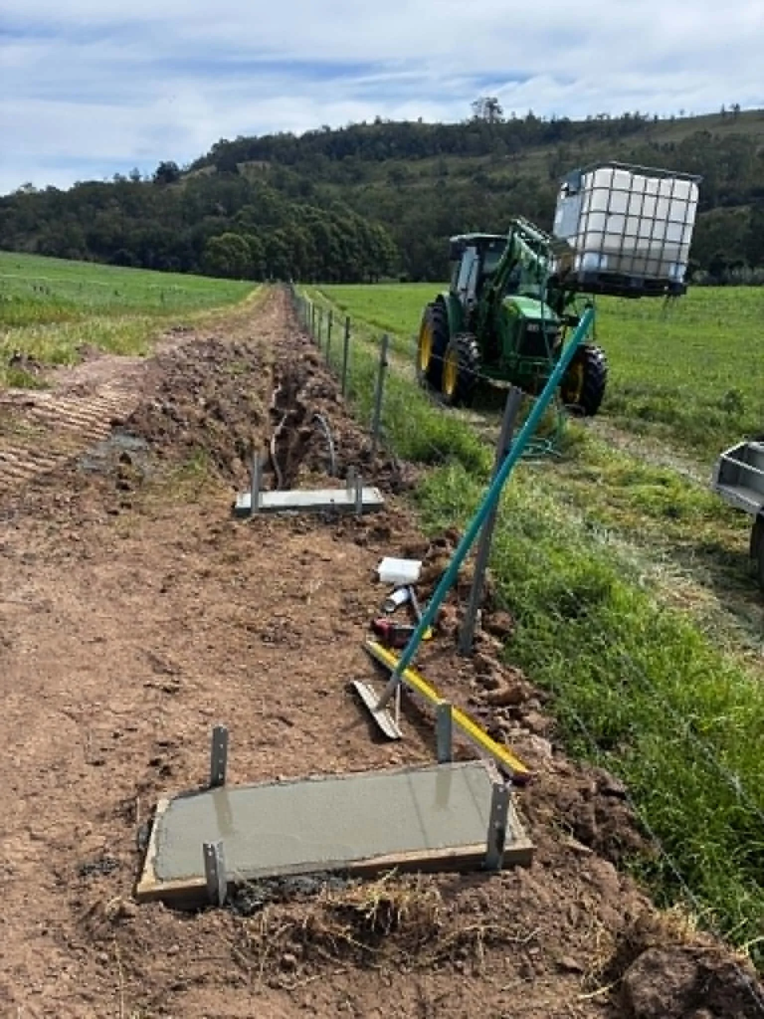 A tractor on a farm preparing a planting bed with a clear sky and rolling hills in the background.