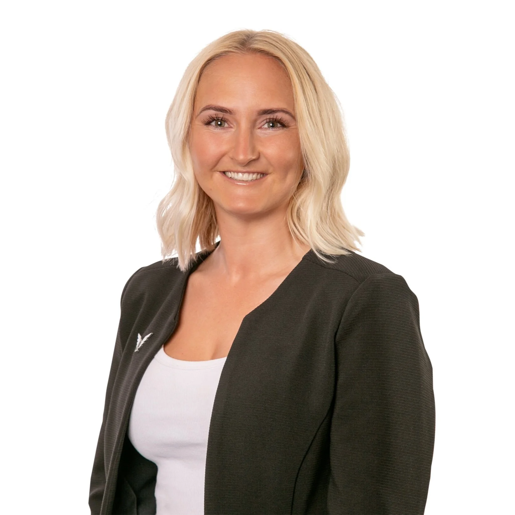 A smiling woman with blonde hair, wearing a black blazer over a white top, standing against a plain white background.