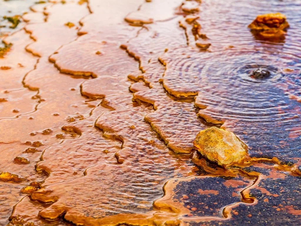 Close-up of a rusty, cracked surface with water and rocks, possibly an old structure or ground.