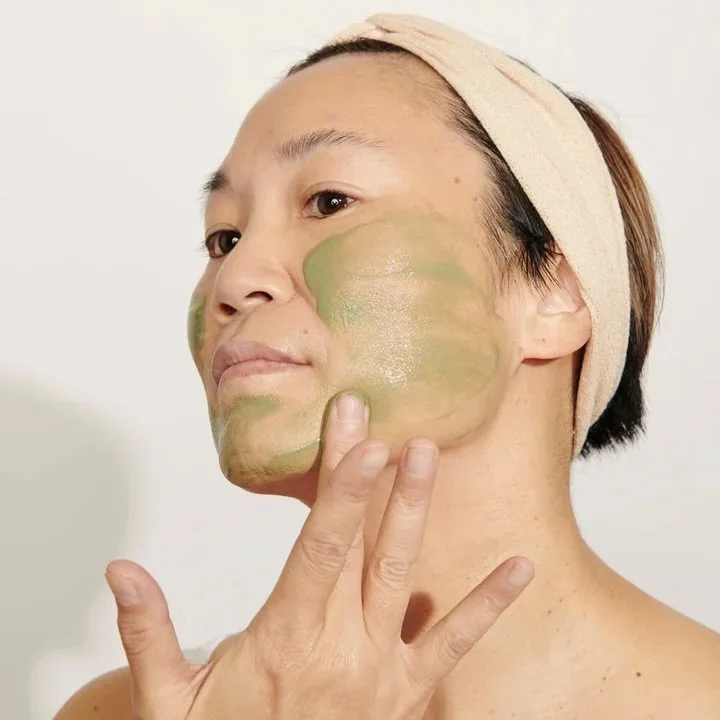 An asian woman is applying a green skincare mask.