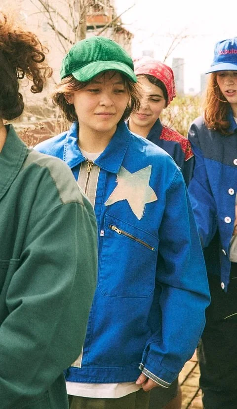 An asian woman is wearing a green ball cap with a blue jacket with a white star on it. She's standing between 3 other people.