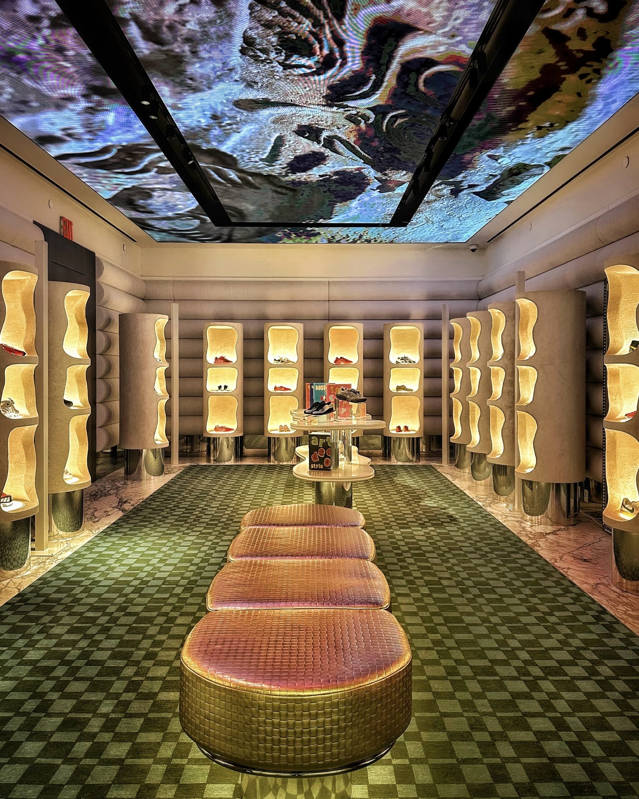 A futuristic shoe store with golden display niches lining the walls, featuring a dramatic digital ceiling projection of swirling, colorful patterns.