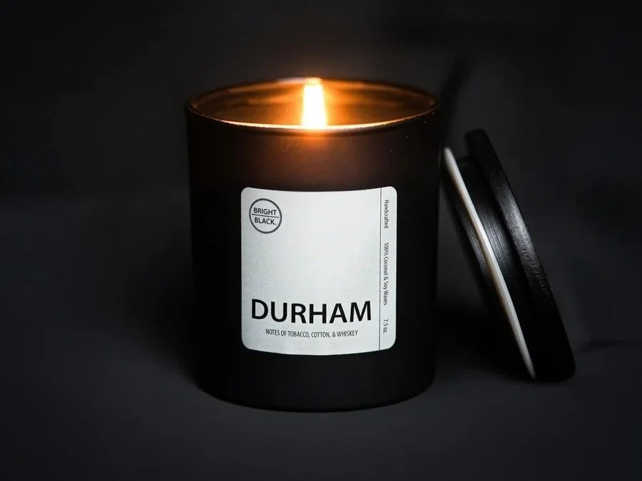 A black candle with white labeling on a black background.