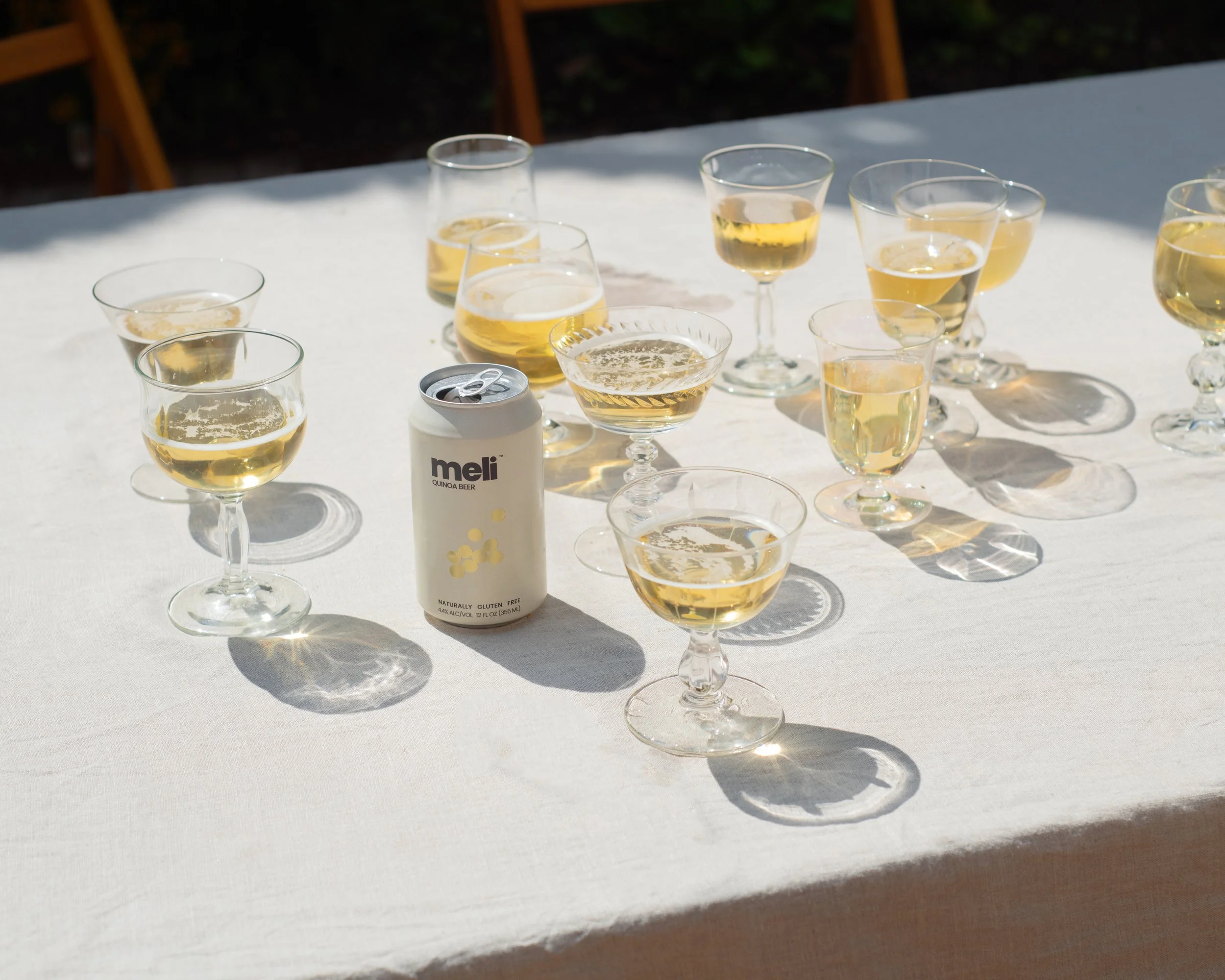 a beer can is in the center of a table with a white table cloth. It's surrounded by glasses filled with beer.