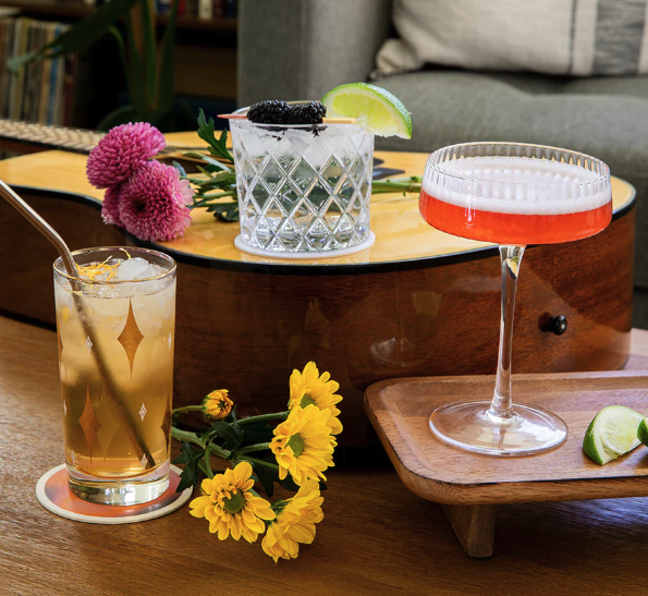 3 drinks are positioned on a wooden coffee table and guitar with flowers around them.