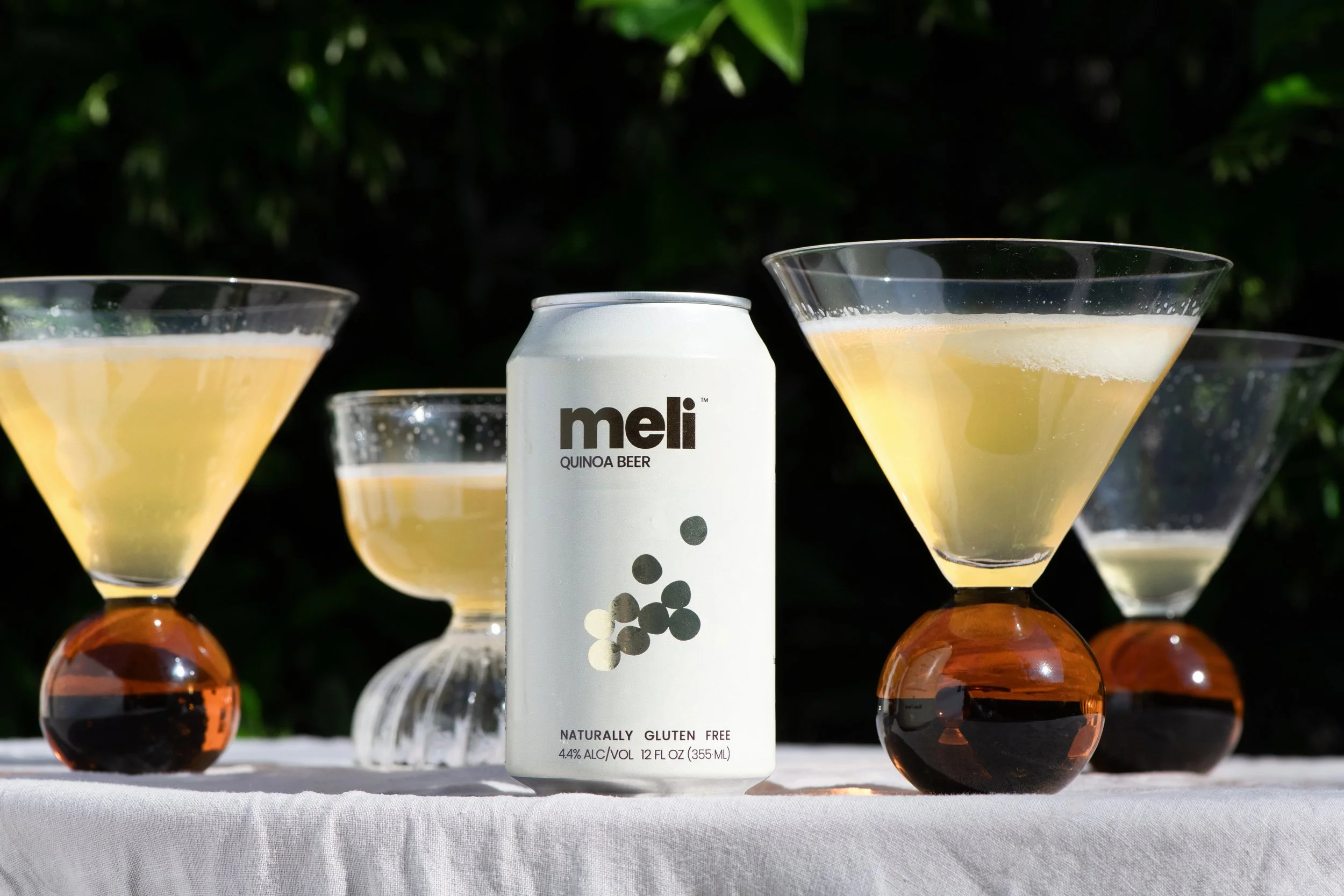 A white beer can on a table surrounded by wine glasses filled with beer on a white table cloth.