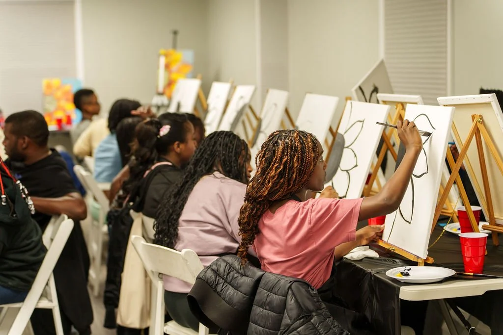 Children painting large flower outlines on canvases at an art class.