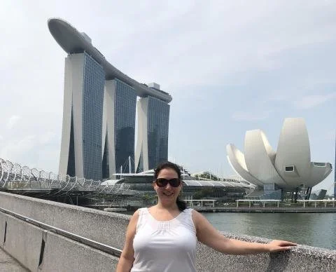 A woman standing on a waterfront walkway with the Marina Bay Sands hotel and ArtScience Museum in Singapore in the background.