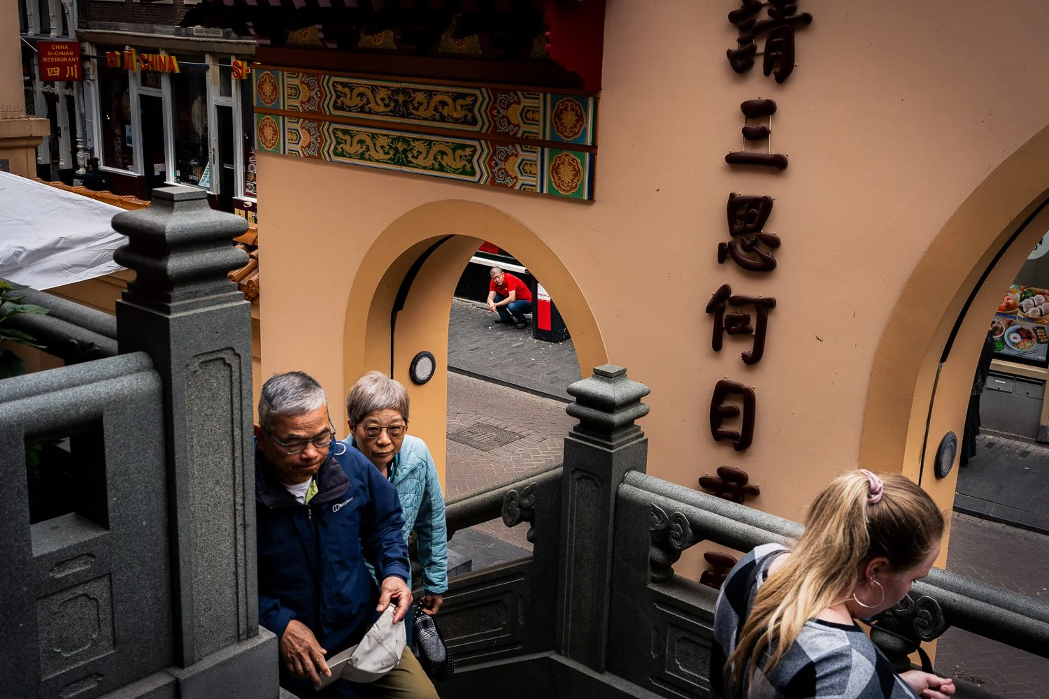 People walking up a staircase outside a building with traditional Asian architectural details and Chinese characters on the wall.