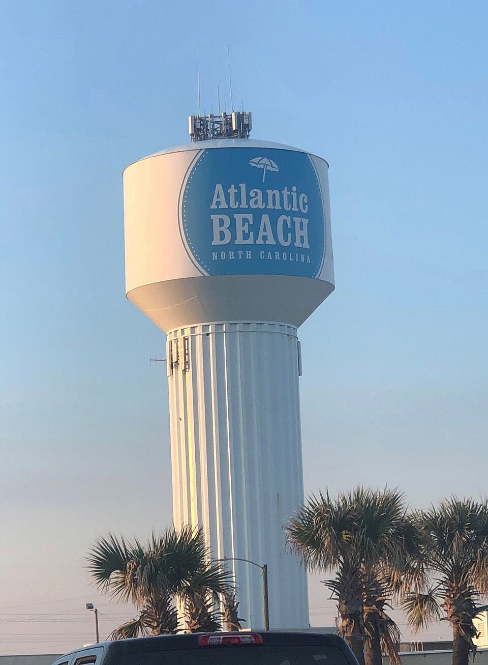 Water tower with Atlantic Beach North Carolina sign, palm trees, and a car at the bottom.