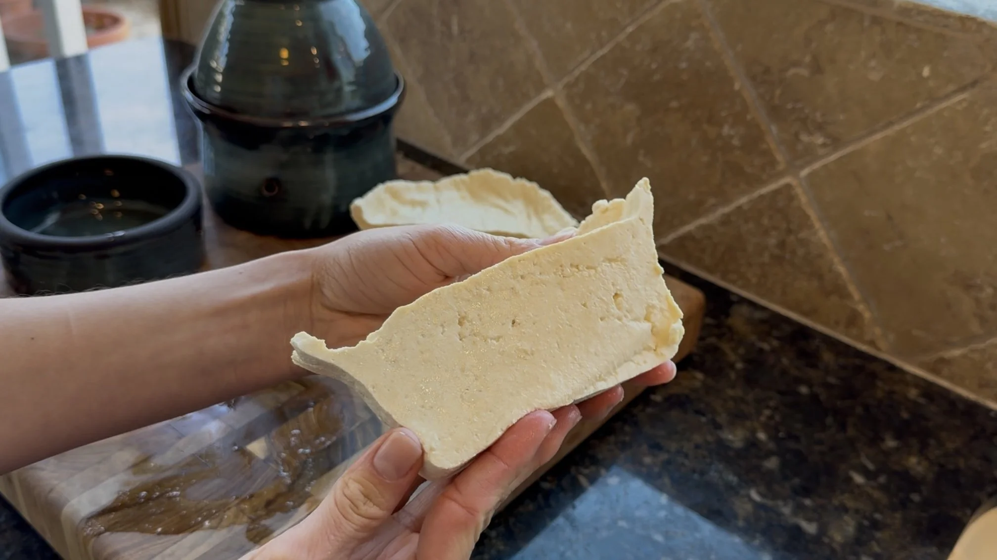 A slice of fresh homemade tofu, with the Thika tofu mold behind it