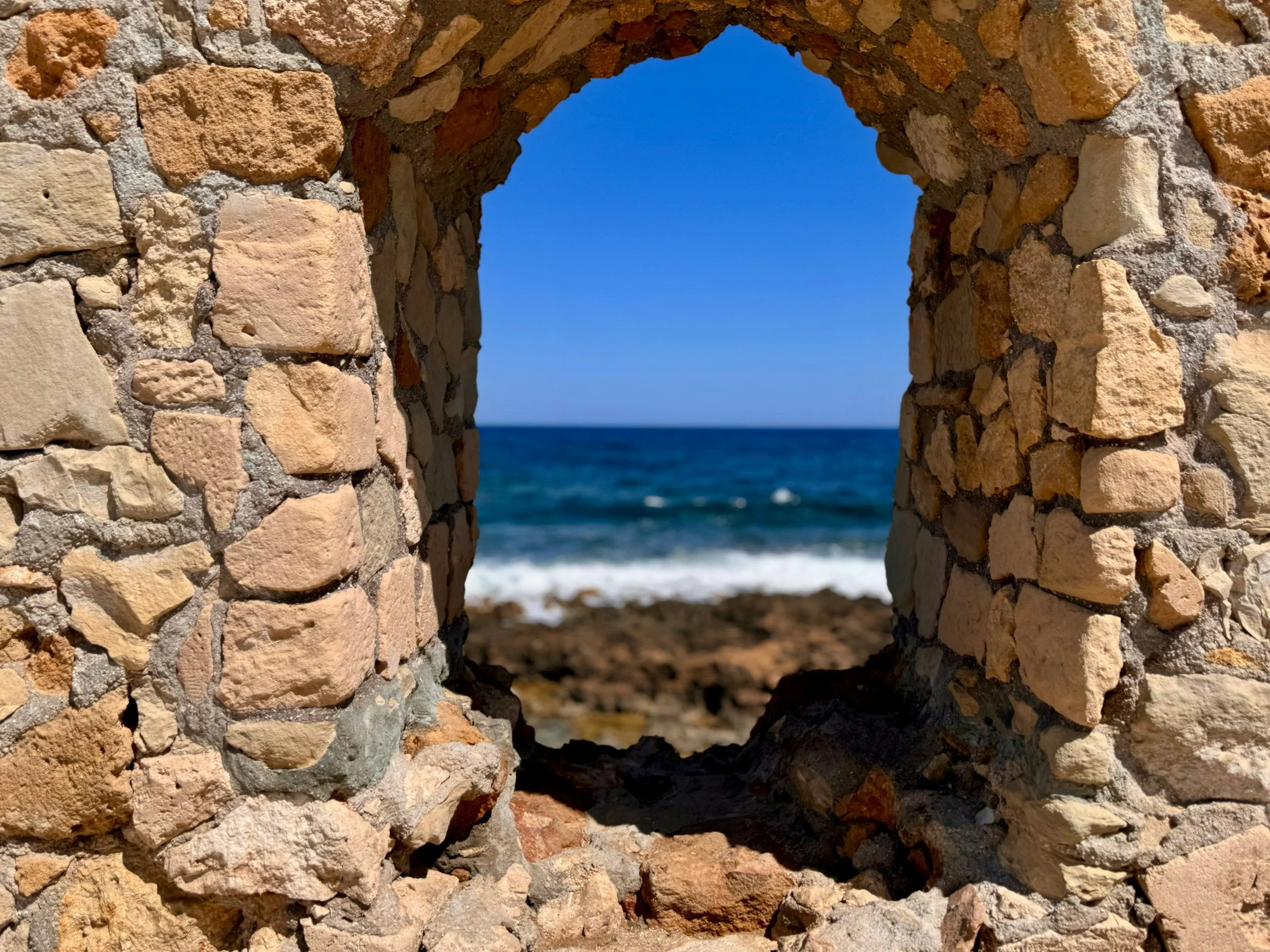 A stone wall with a circular window revealing the ocean and blue sky