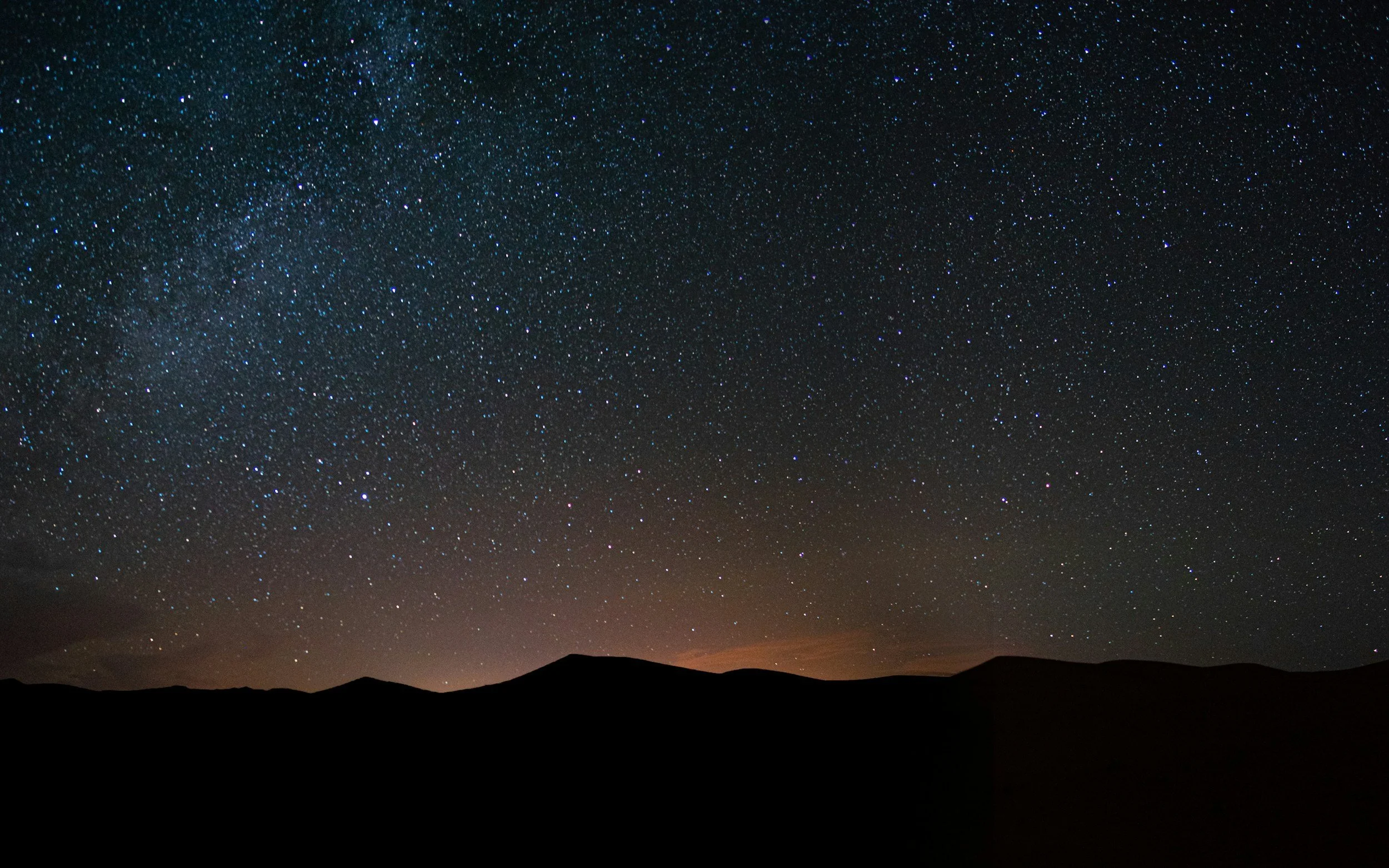 Night sky filled with stars over a silhouette of mountains.