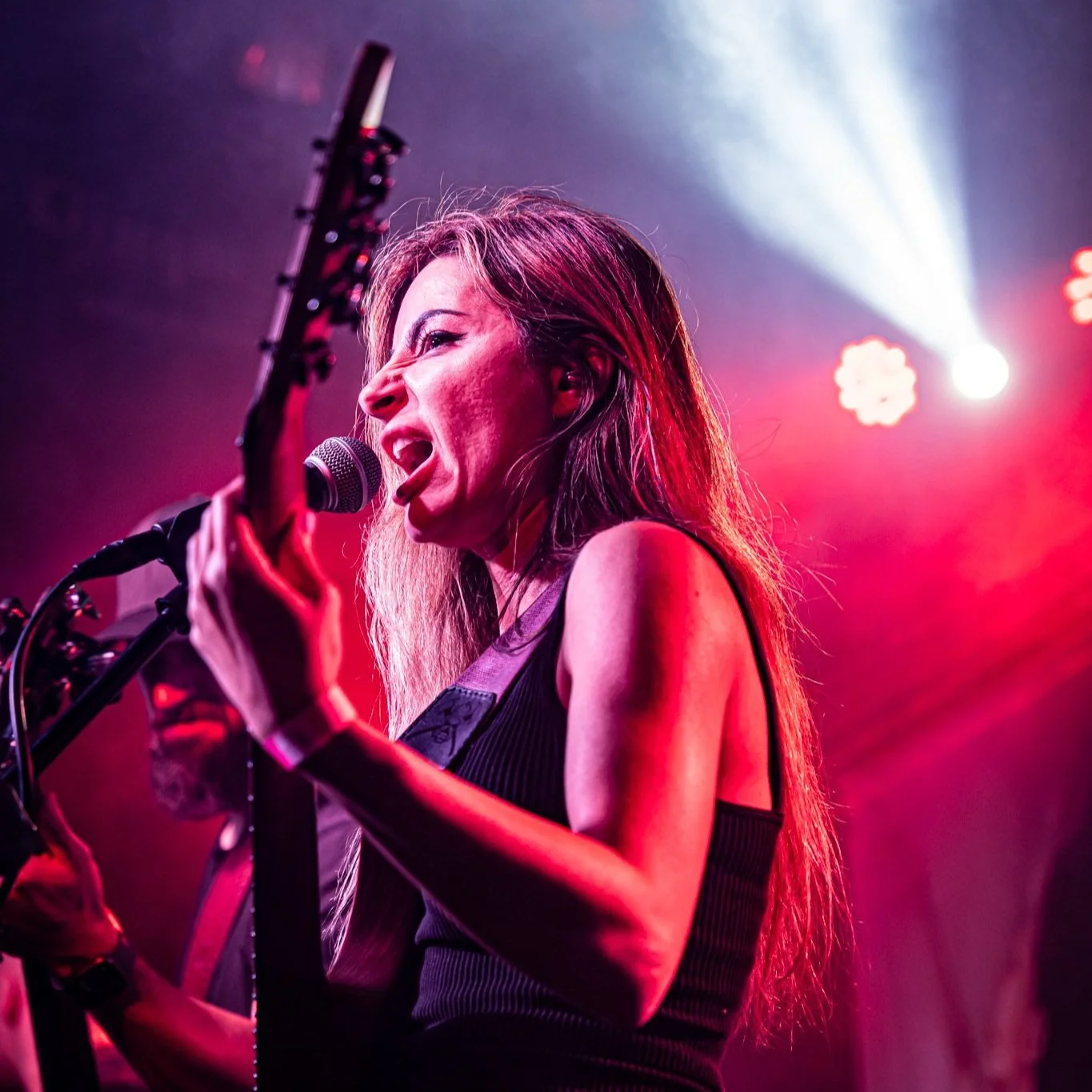 A woman singing and playing guitar on stage with bright pink and red stage lighting.