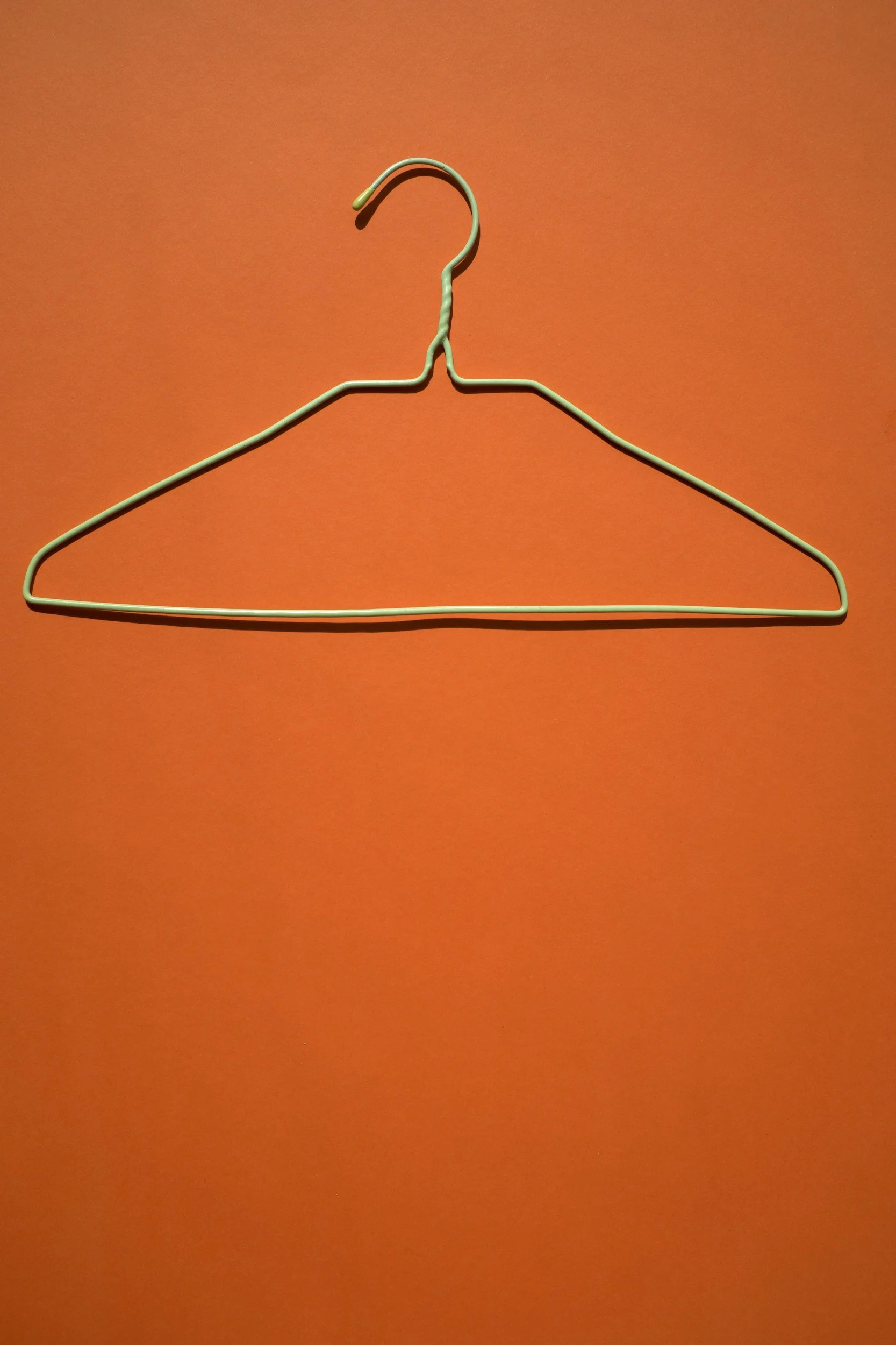 A white wire coat hanger hanging against an orange background.