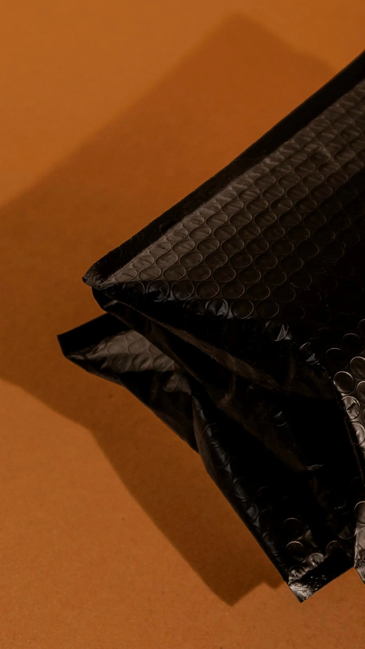 Close-up of a black bubble wrap envelope against a beige background.