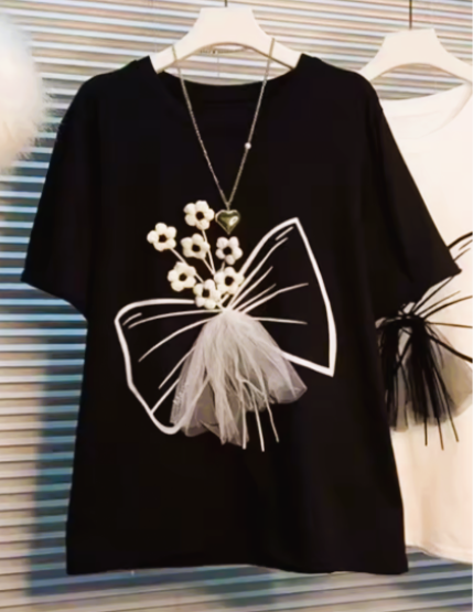 Black T-shirt with white floral and bow design, accessorized with a silver necklace featuring a green heart pendant and a small white fluffy pom-pom.