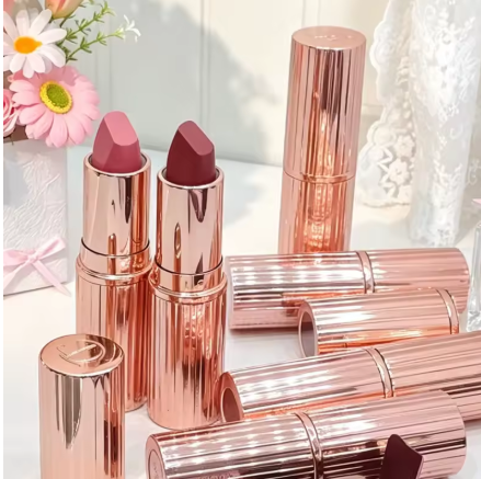 Metallic pink lipstick tubes with some open lipsticks and flowers in the background.