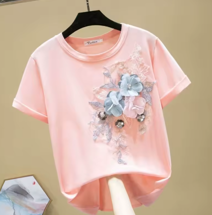 Pink T-shirt with floral embroidery and decorative embellishments hanging on a black hanger.