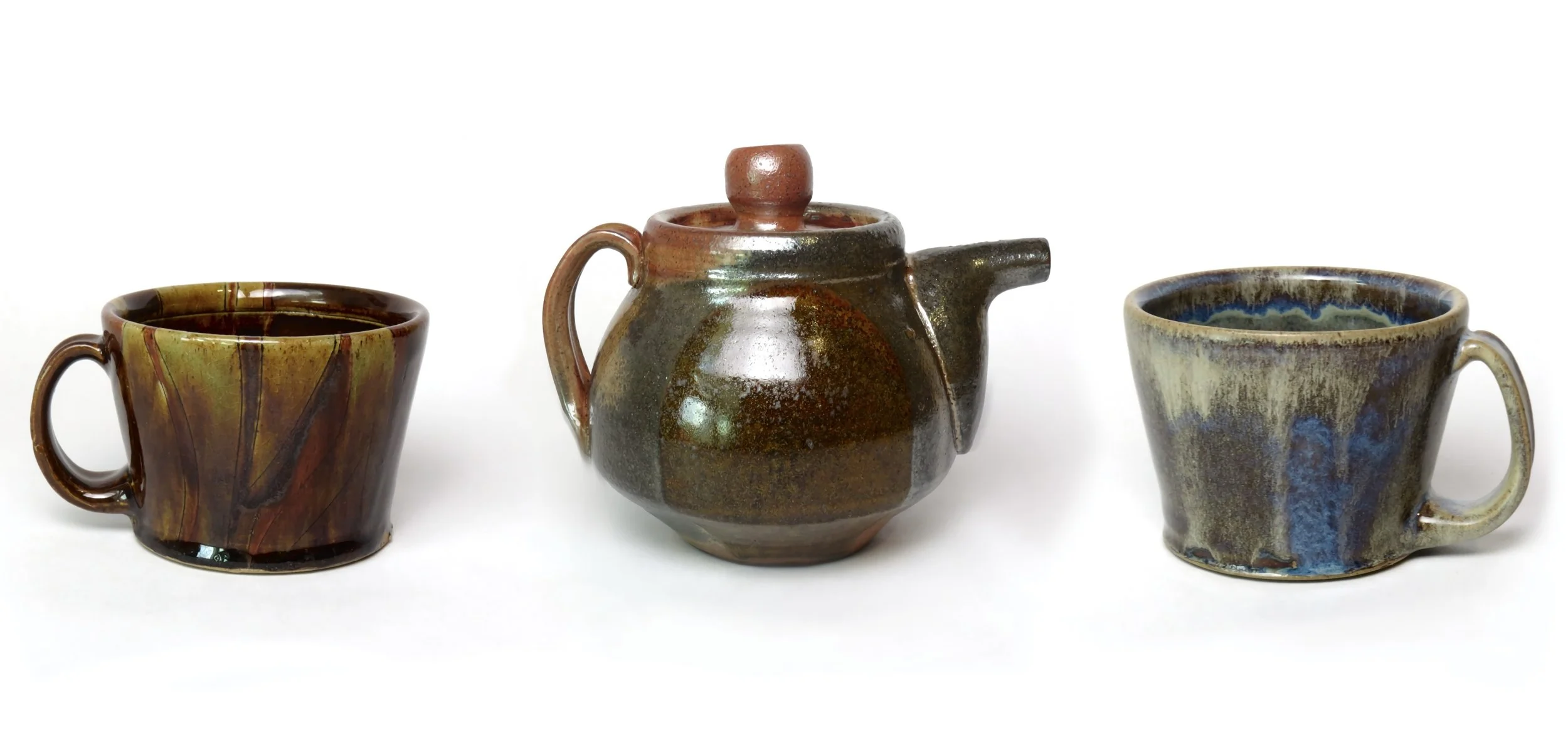 Three ceramic pieces: two mugs and a teapot, all with earthy, glazed finishes on a white background.