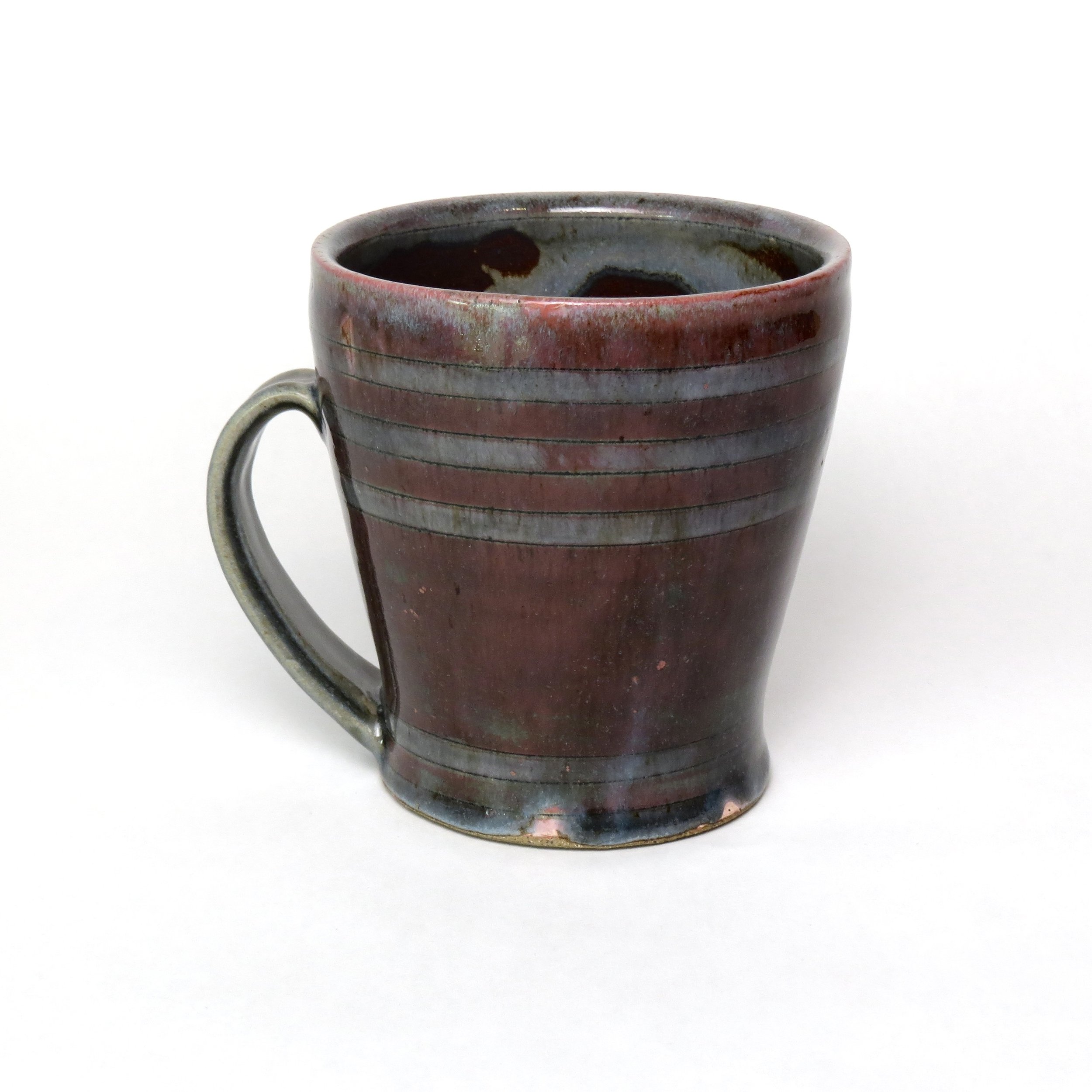 A ceramic mug with a striped red and brown glaze, filled with a dark liquid, set against a plain white background.