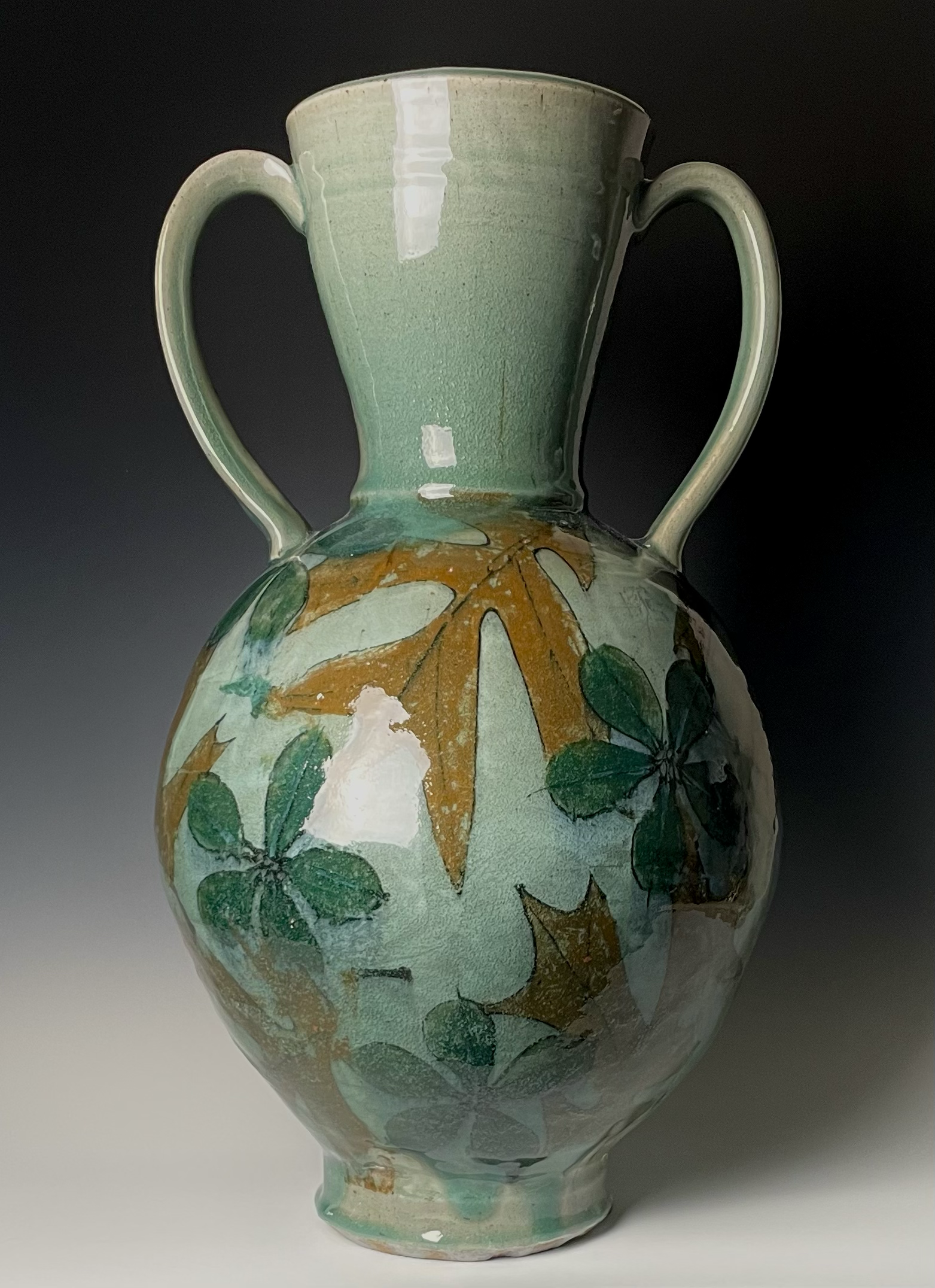 A ceramic vase with a floral design featuring large orange leaves and green leaves, glazed in shades of green and cream.