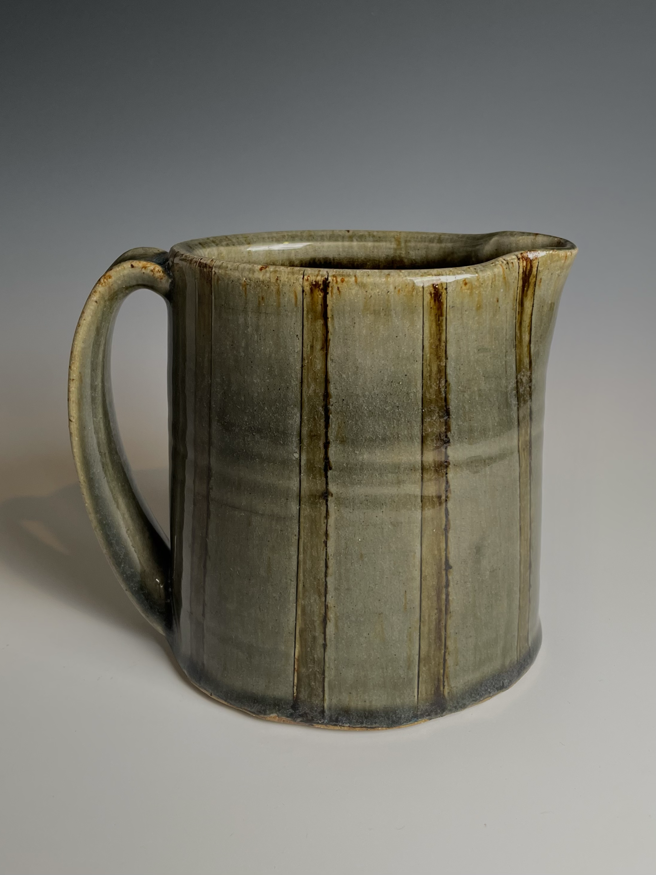 A ceramic mug with vertical brown and gray glaze drips on a light gray background.
