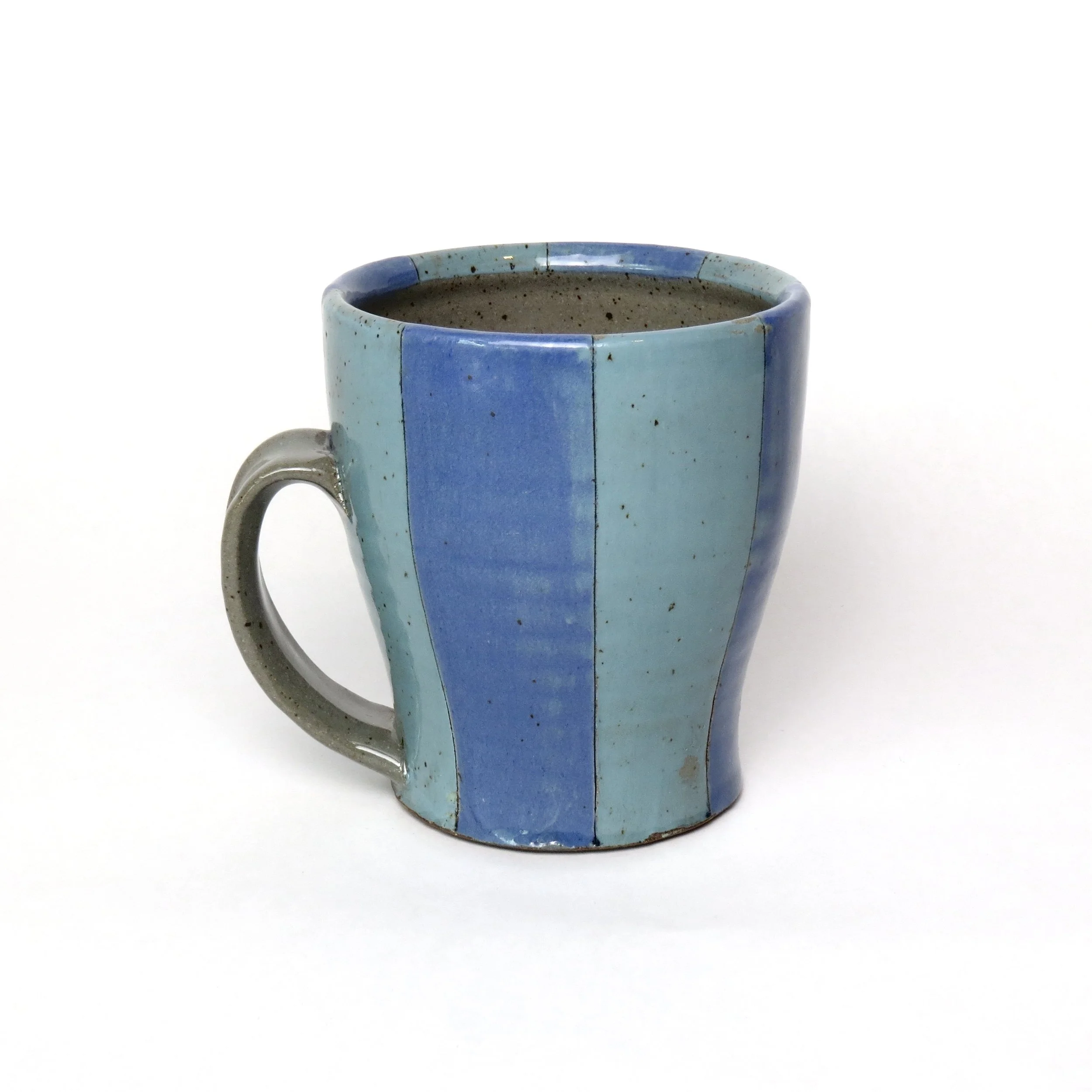 A blue ceramic mug with a speckled beige interior, sitting on a white surface with a plain white background.