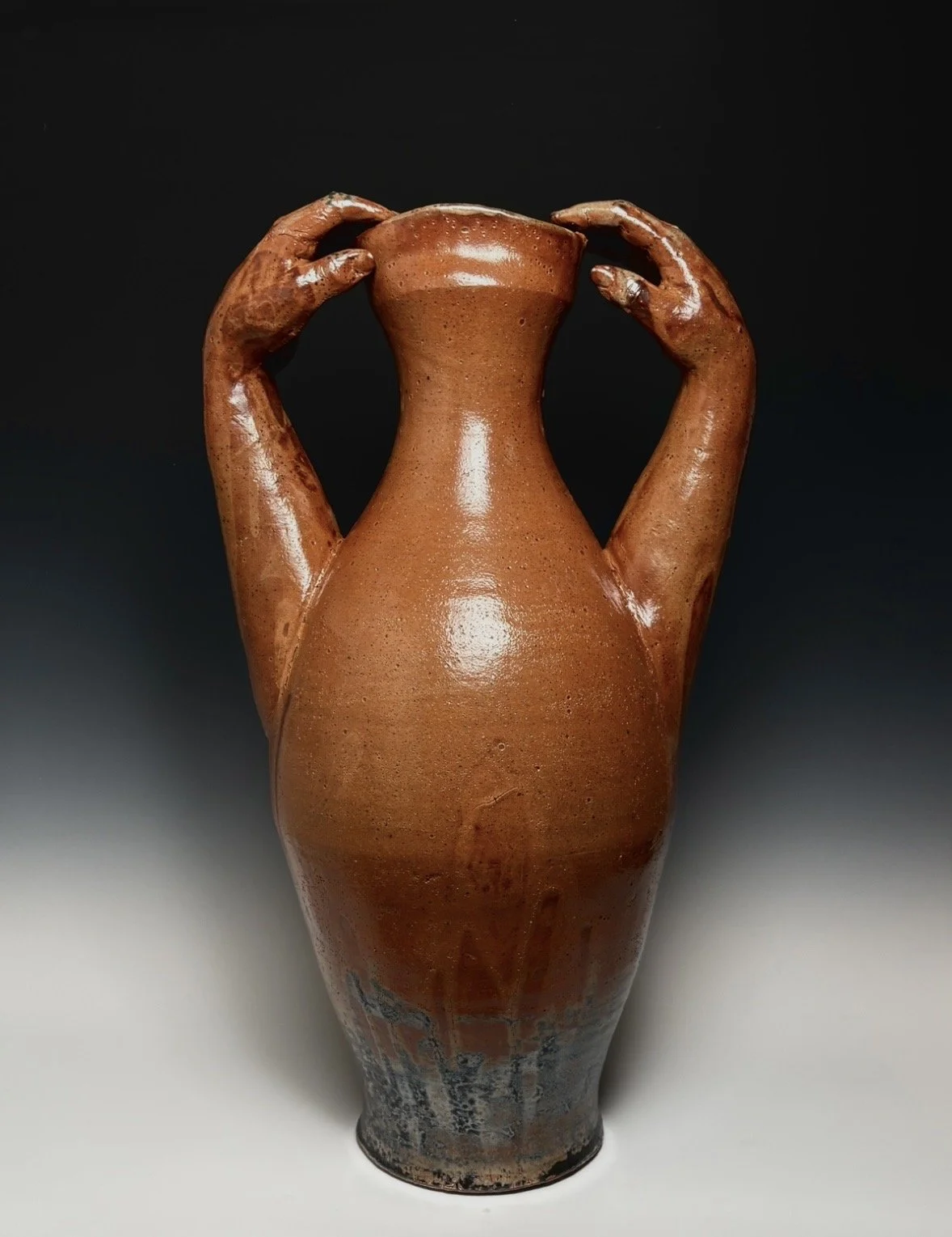 Clay pottery with a tall, slender body and two handle horns, set against a dark background.