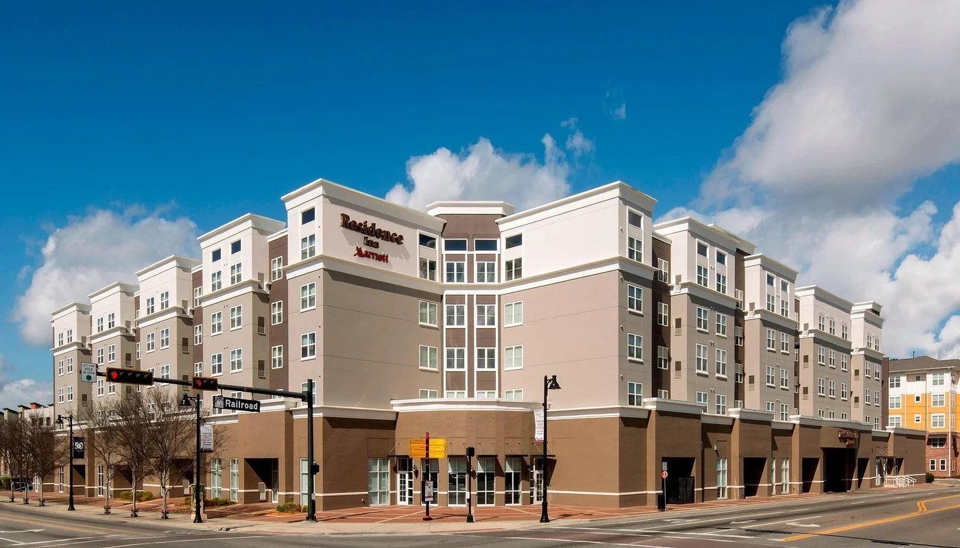 Exterior view of a multi-story Residence Inn hotel at the corner of a city street on a partly cloudy day.