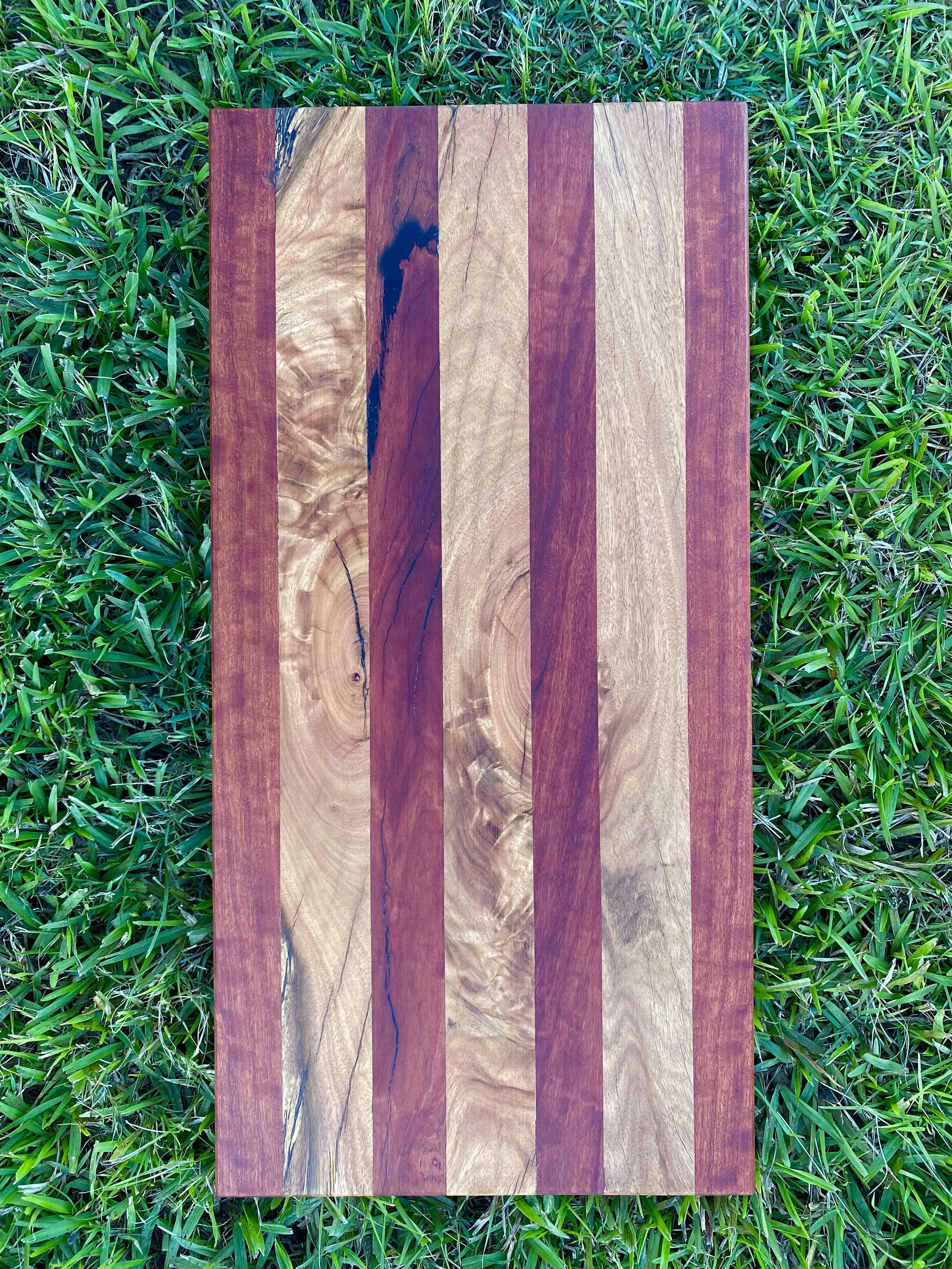A wooden cutting board with alternating light and dark wood stripes, placed on green grass.