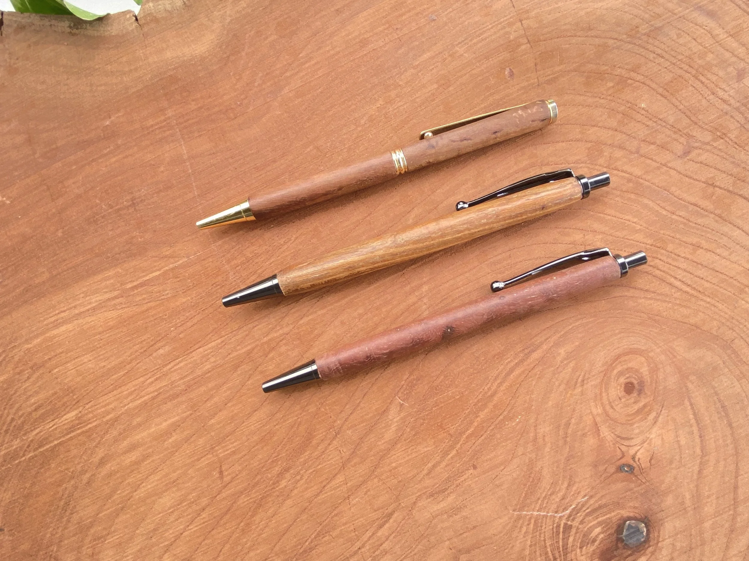 Three wooden ballpoint pens with metal clips and tips lying on a wooden surface.
