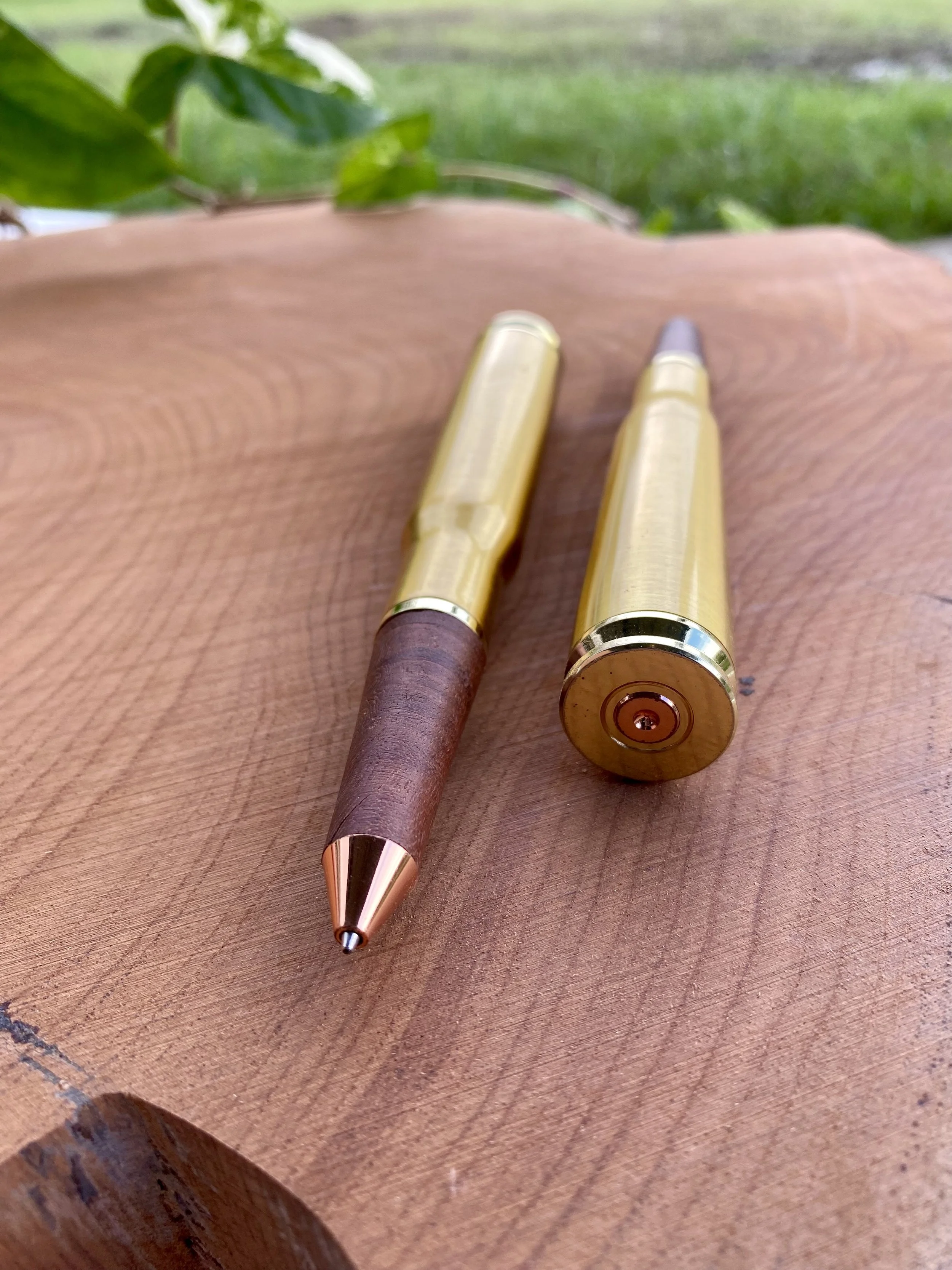 Two pens with gold-colored bodies, one with a wooden barrel and the other with a metallic tip, resting on a wooden surface.