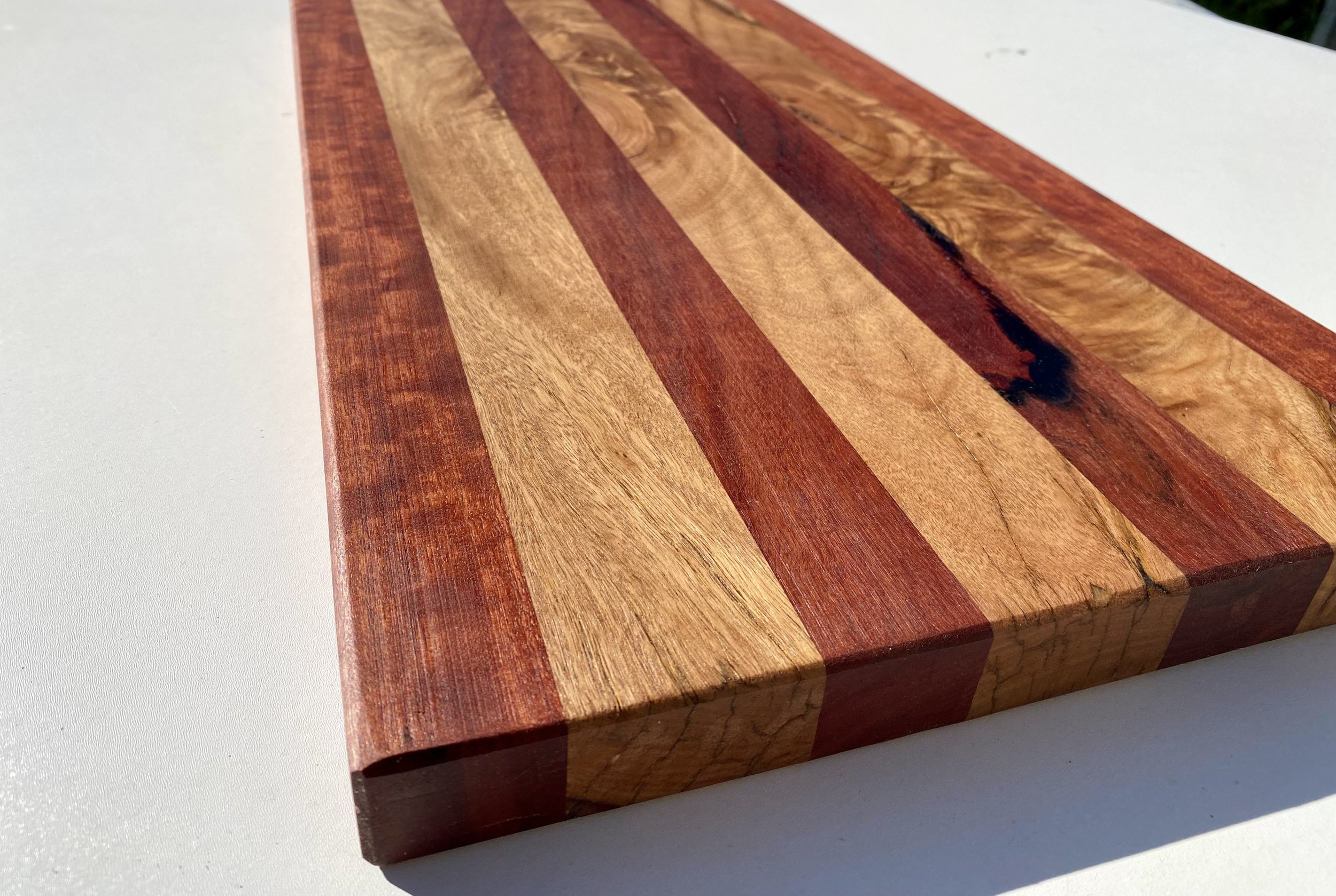 Close-up of a wooden cutting board with alternating light and dark wood stripes on a white surface.
