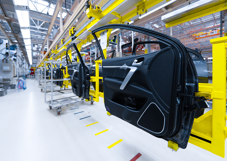 Car doors on assembly line in an automotive manufacturing plant with yellow scaffolding and industrial equipment.
