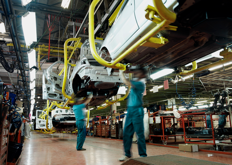 Automobile assembly plant with workers installing car bodies on an automated conveyor system.