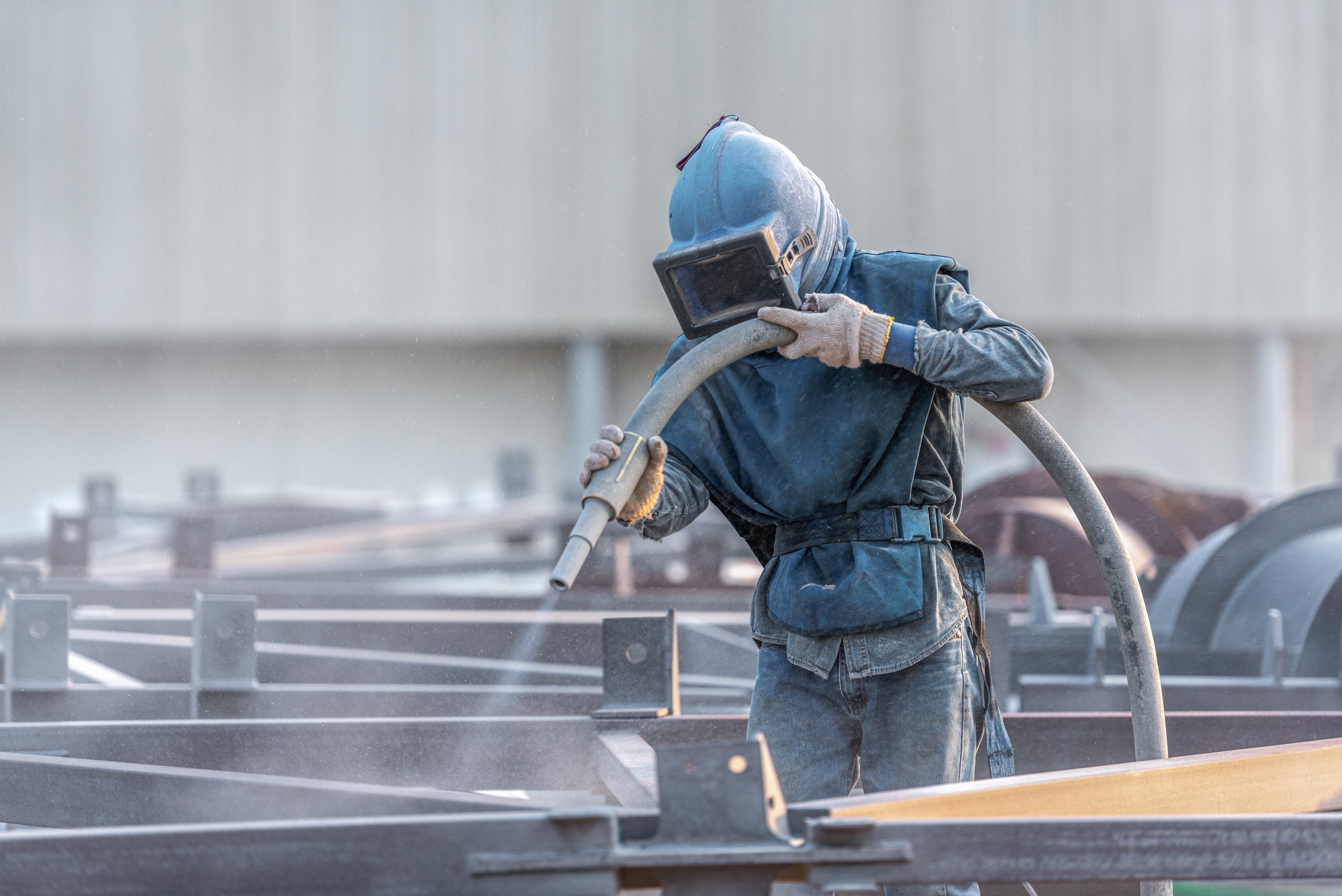 Worker welding metal structure at construction site, wearing protective helmet and gloves, with welding hose.