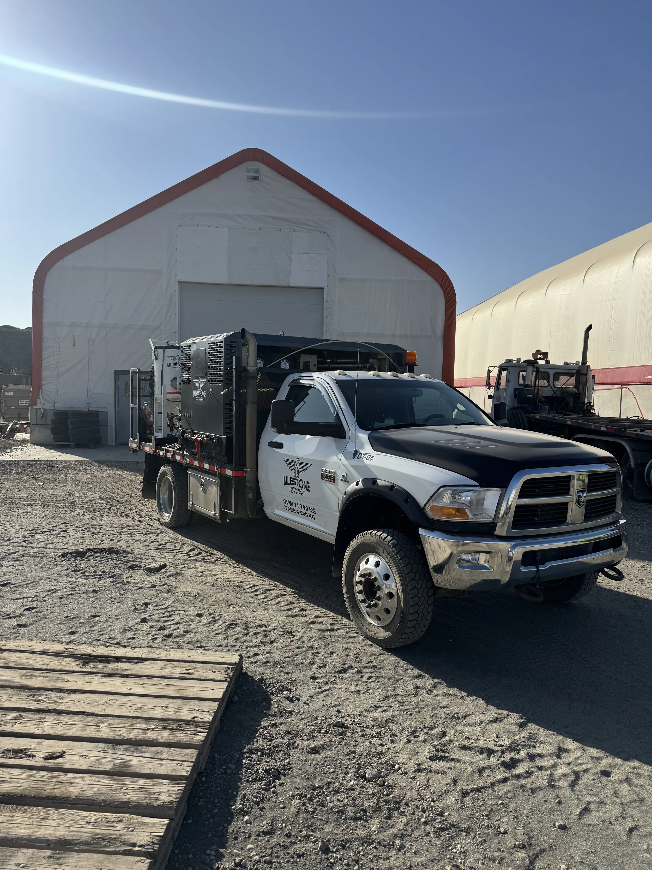 A white and black utility truck parked outside a large white industrial building with a red trim, under a clear blue sky.