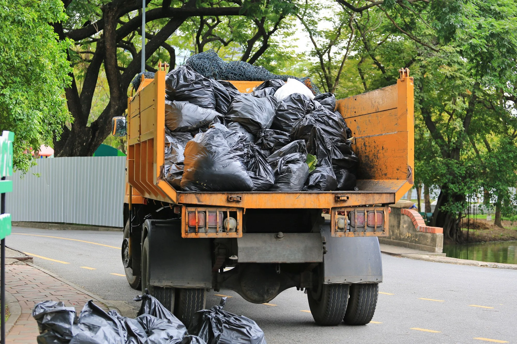 A yellow dump truck filled with black garbage bags parked on a suburban street.