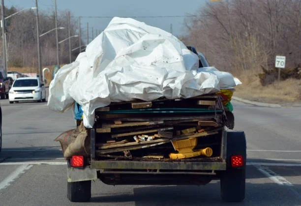 A truck hauling construction debris on a two-lane road with traffic in the background.