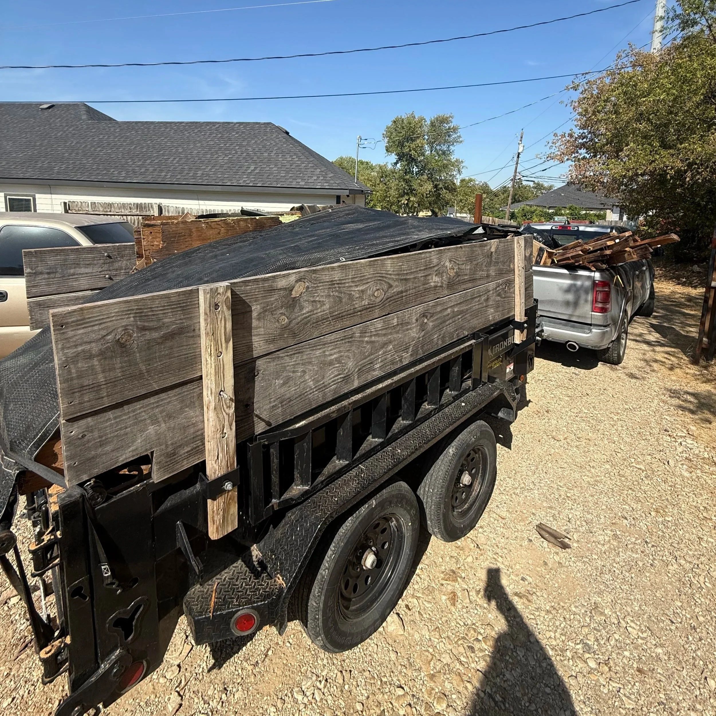 A garbage truck lifting a blue recycling bin to empty its contents into the truck on a residential street with trees and brick houses in the background.